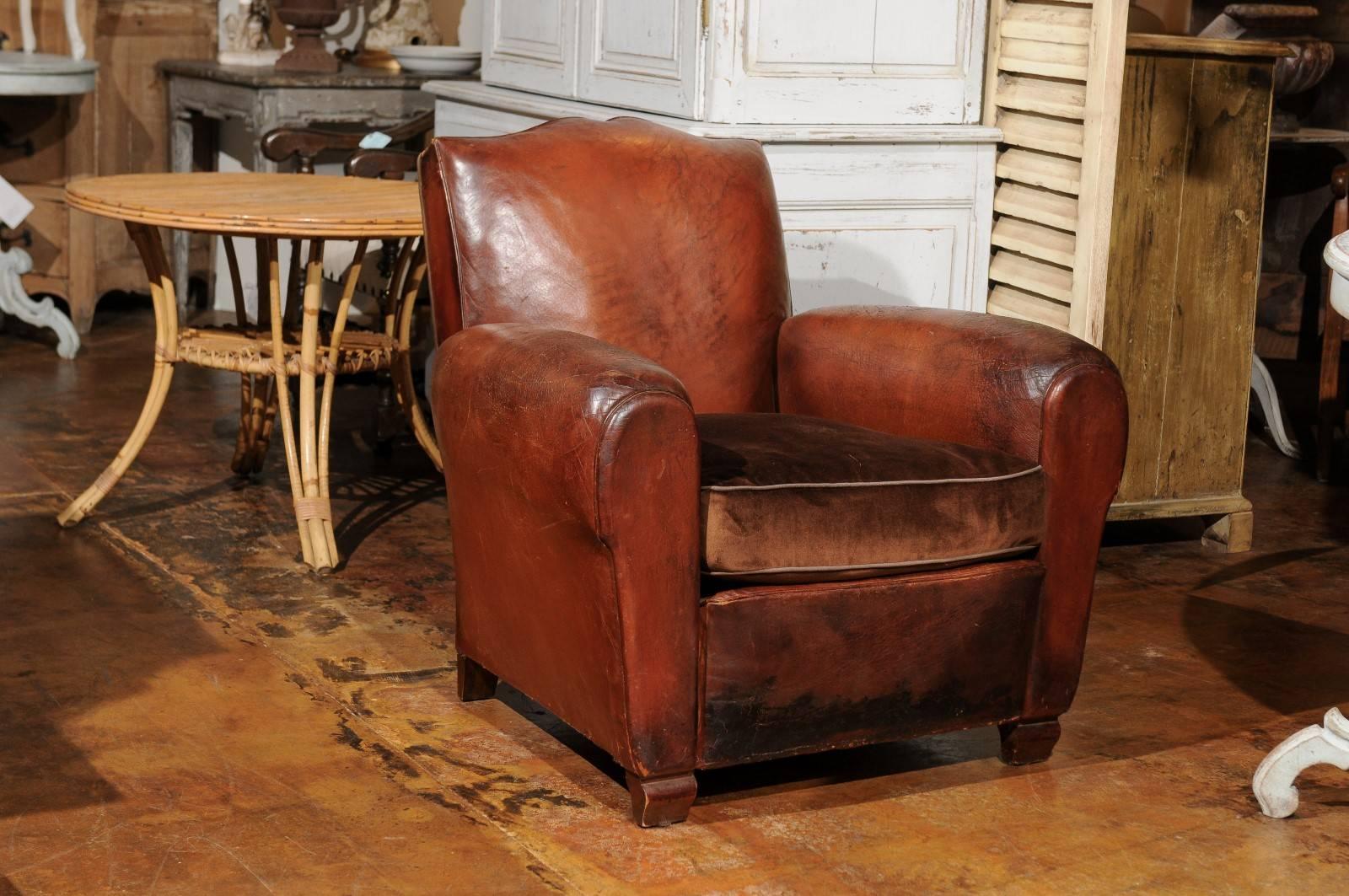 A pair of French leather club chairs with brown velvet seat cushion from the early 20th century. Each of this pair of French club chairs was made in the 1910s and features a slightly slanted back, perfect to receive the sitter comfortably. Each seat