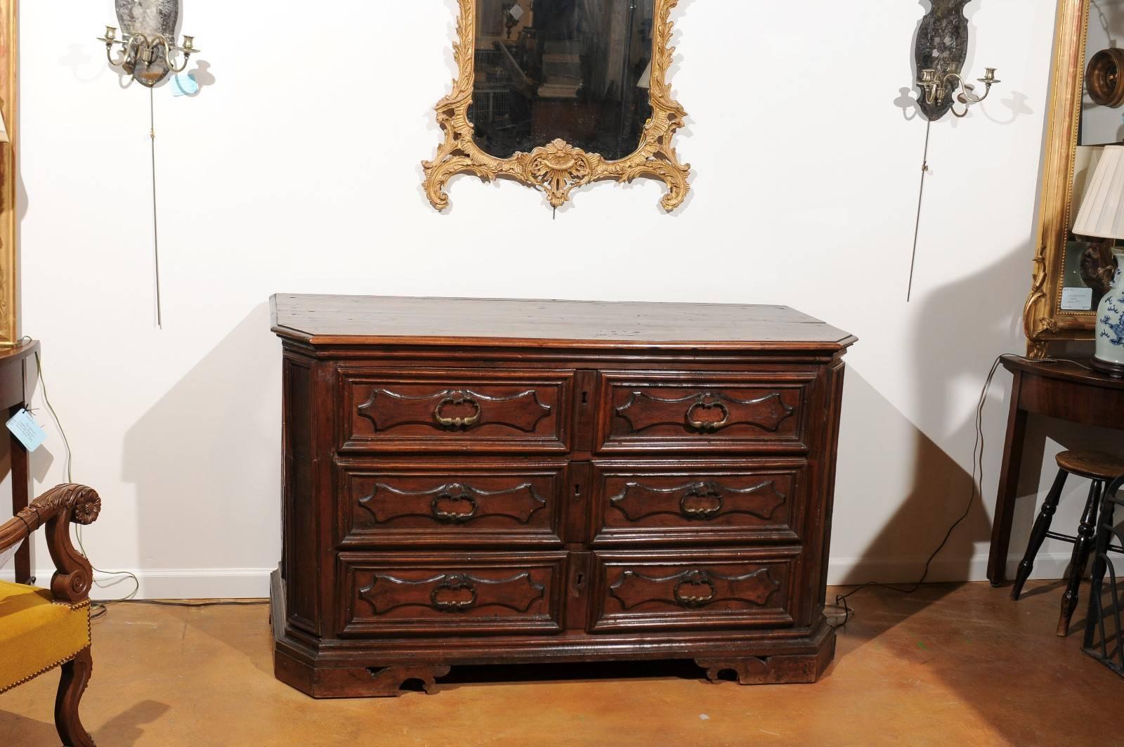 An Italian dark walnut three-drawer commode with cartouches and diamond motifs from the mid 19th century. This Italian commode features a rectangular top with beveled edges and chamfered corners in the front, sitting above three long drawers adorned