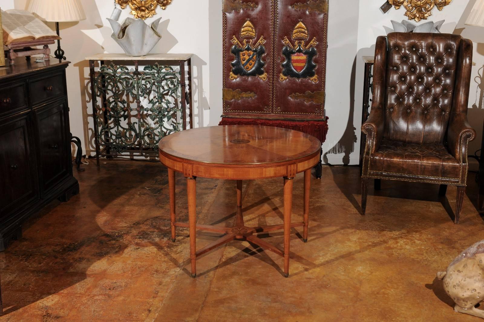 A French round burled walnut inlaid center table with brass trim and cross stretcher from the late 19th century. This French side table was born in the 1880s, a decade after the fall of the Emperor Napoleon III. Featuring an exquisite circular top