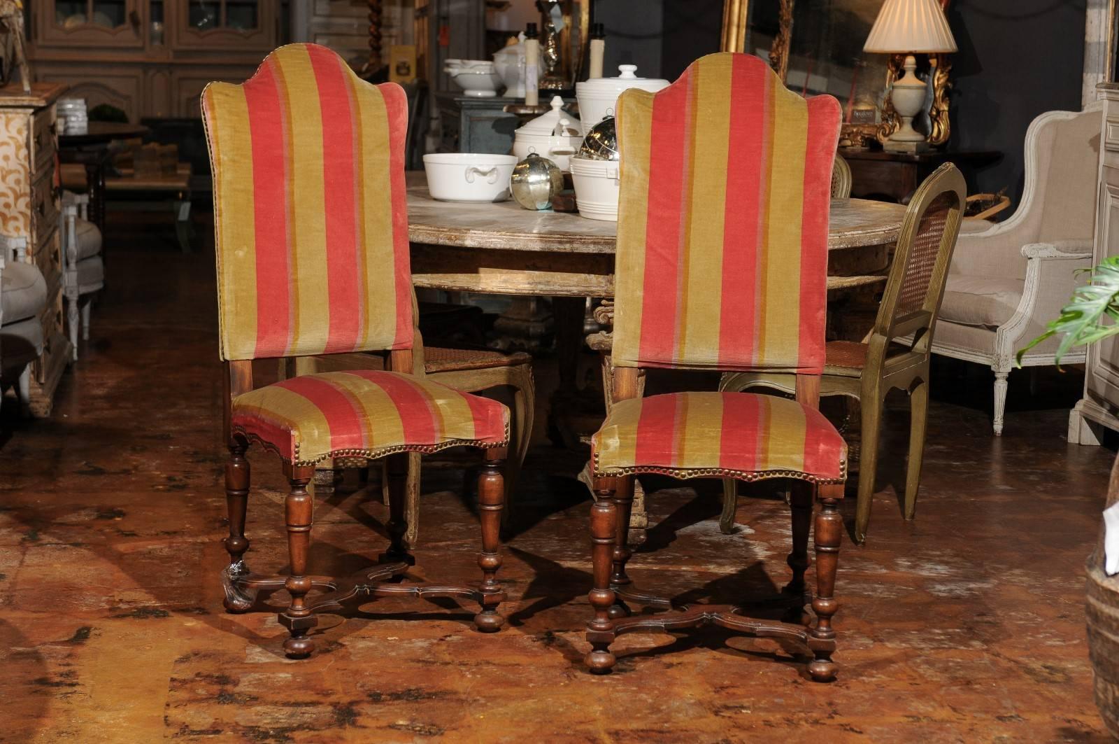 A set of four Italian tall camelback upholstered dining room side chairs with X-form stretcher from the late 19th century. Each of this set of Italian dining chairs features a tall and slightly slanted camel back and a seat decorated with a