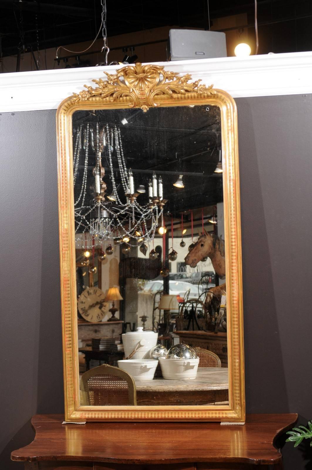 A tall French giltwood Rococo style mirror with carved crest from the late 19th century. This French mirror features an exquisite rocaille carved crest, reminiscent of the decorative motifs so praised under the reign of Louis XV. This gilt crest