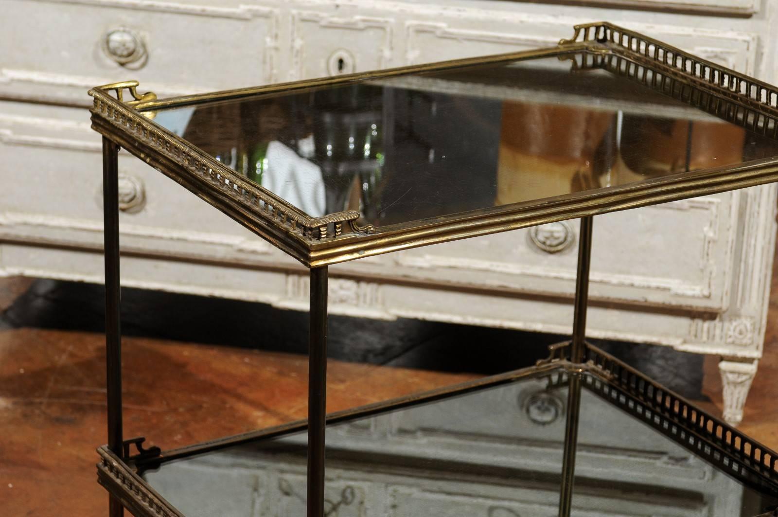 A continental two-tiered brass trolley with mirrored shelves and casters from the early 20th century. This tiered cart features two rectangular shelves, each adorned with a mirrored top surrounded on both sides by a delicate pierced brass gallery