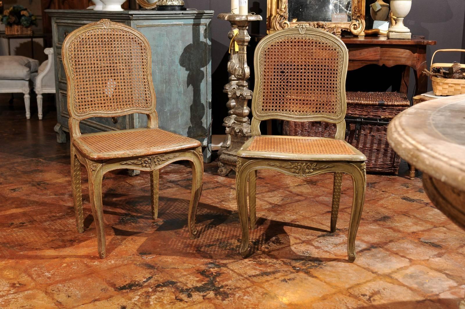 A set of four French Louis XV style painted wood and cane dining room chairs from the late 19th century. Each of this set of French chairs features a slightly slanted back with subtle curves, adorned on the upper rail with a delicately carved floral