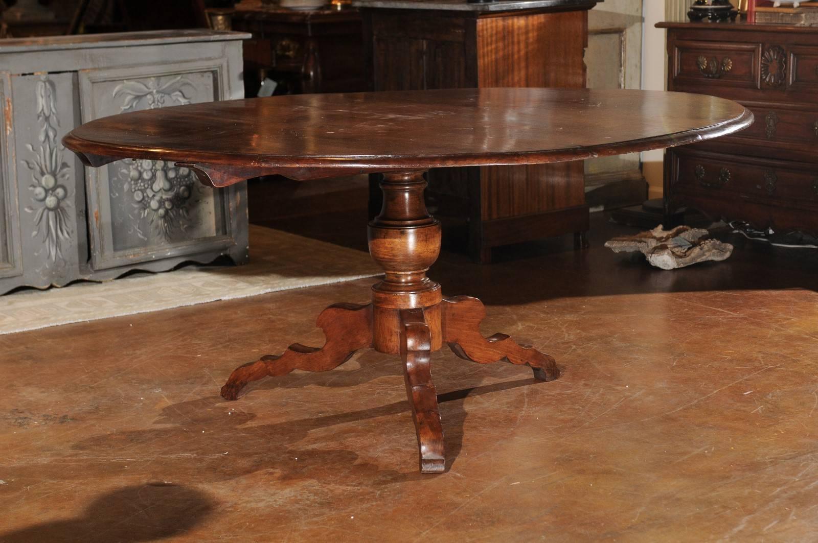 An Italian walnut dining room table with round top and pedestal base from the second half of the 19th century. This Italian pedestal table features a circular top with rounded edge, sitting above a turned pedestal base, raised on tripod legs. The