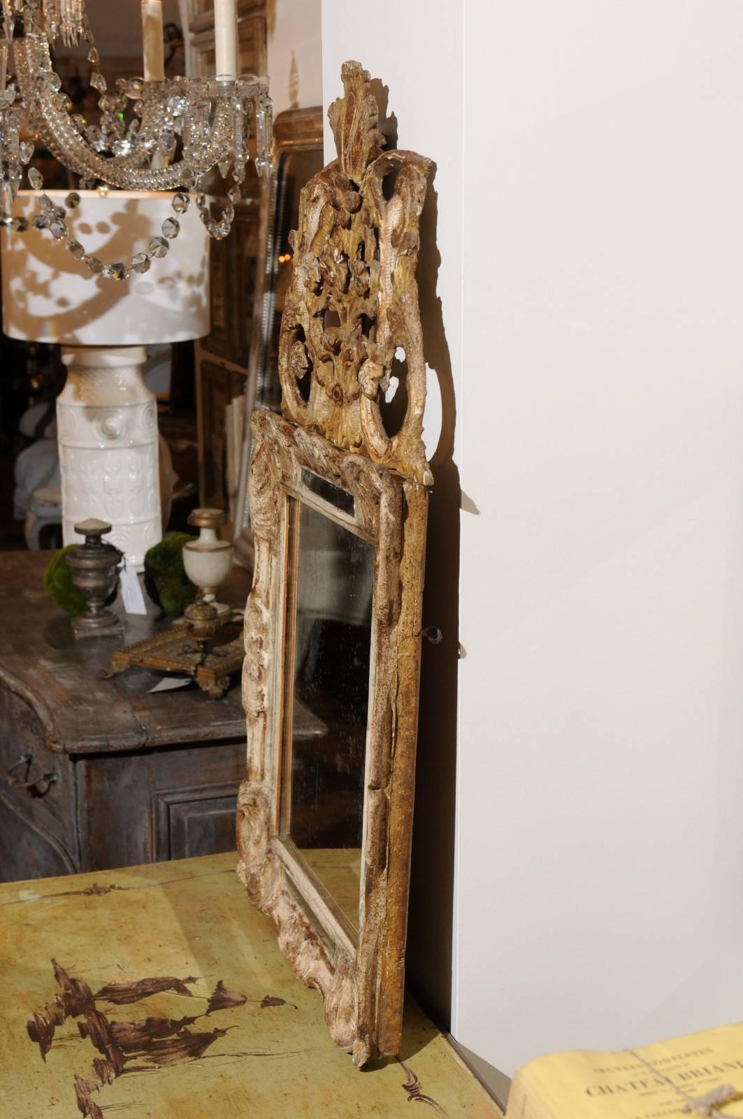 A French mid-19th century gilt and painted Louis XV style mirror with detachable carved crest. This small French mirror features an eye-catching carved crest adorned with various volutes and acanthus leaves delicately flanking central flowers and