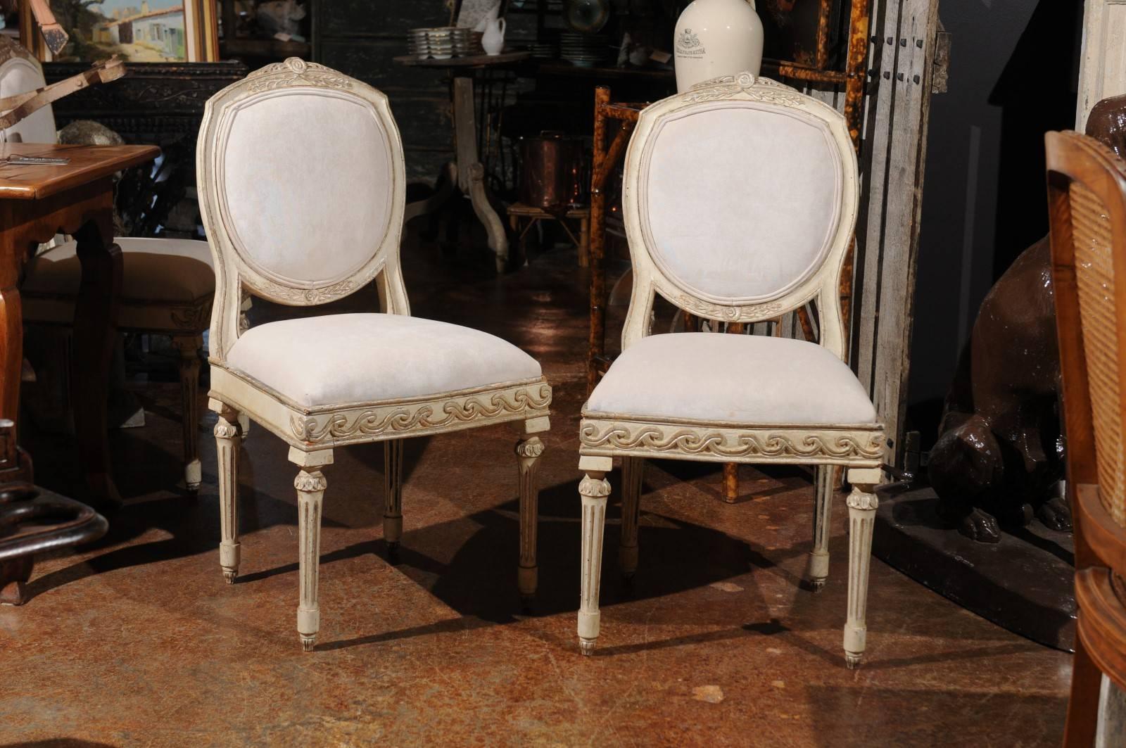 A set of six French neoclassical style painted and silver parcel-gilt dining room chairs from the 19th century with new upholstery. Each of this set of six French side chairs features an unusually shaped back with new double welt muslin upholstery,