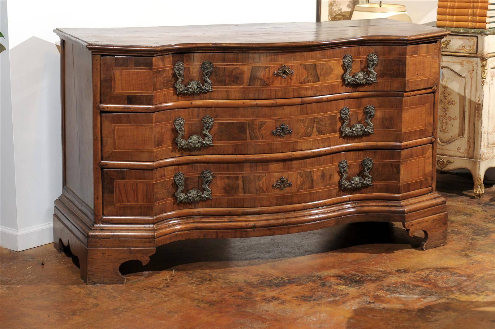 18th century Venetian marquetry inlaid walnut chest, the shaped top surmounting three conforming serpentine drawers with inlay throughout and elaborate pulls above a stepped apron and raised on bracket ogee feet.