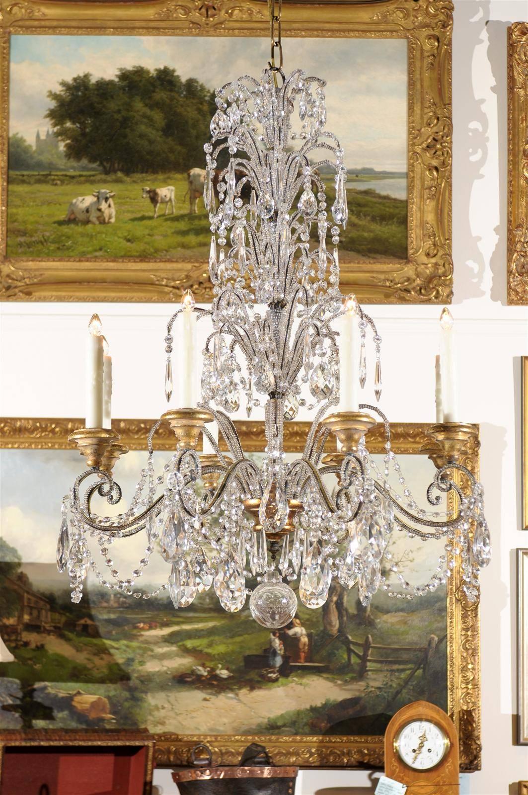 An Italian eight-light crystal chandelier with fountain-like central column and scrolled arms from the 20th century. One cannot but be attracted to the upper section of this crystal chandelier, imitating bustling jets, springing from an imagined
