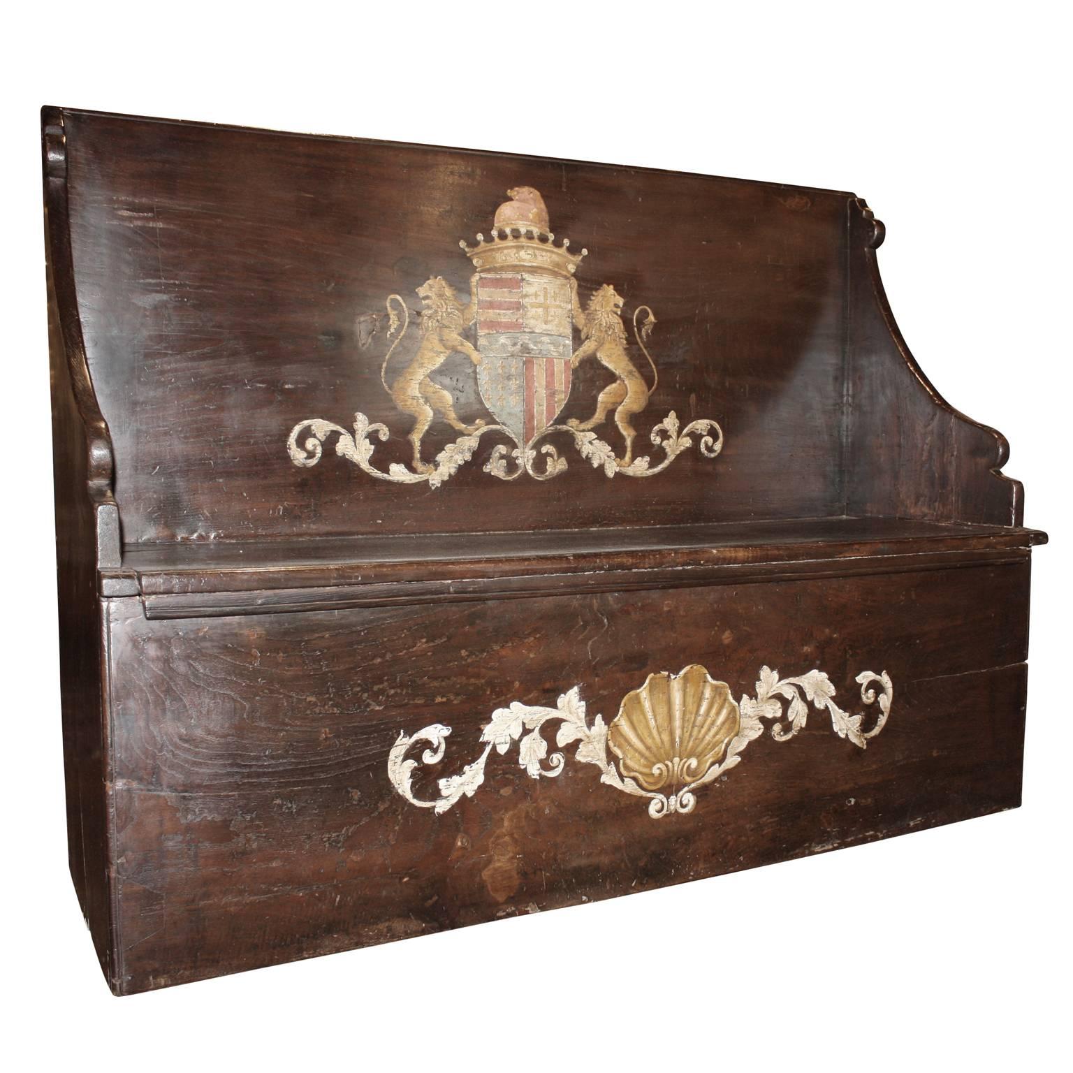 This Italian wooden hall bench from the early 19th century features a tall back, adorned in its center with a family crest made of two lions, flanking the central coat of arms, topped with a crown and a hat reminiscent of that worn by the Doge of