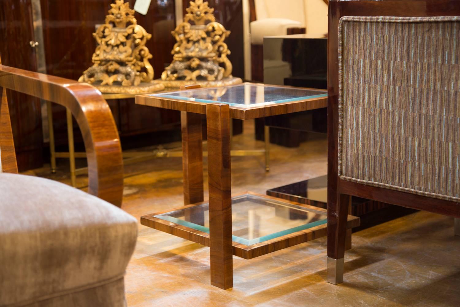 This pair of contemporary two-tiered end tables made of walnut and glass features square shaped beveled glass tops surrounded by beautifully veneered walnut frames. Each table features three straight legs ingeniously placed in various positions with