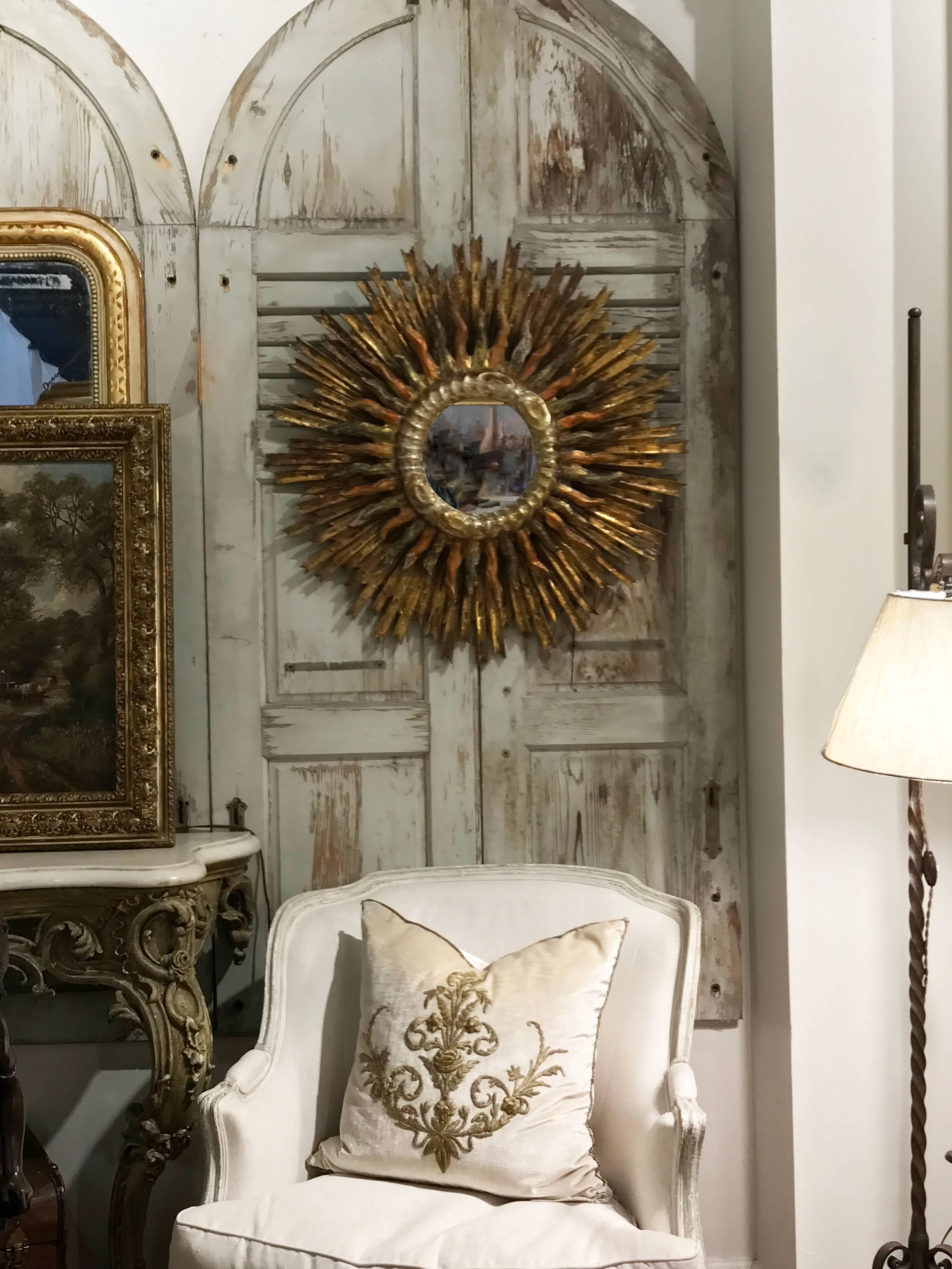 This exquisite Italian painted and gilded double sunburst mirror from the late 19th century features a clear mirror in the center, surrounded by a giltwood molding, reminiscent of wavy clouds. Radiating from the center, two layers of sun rays make