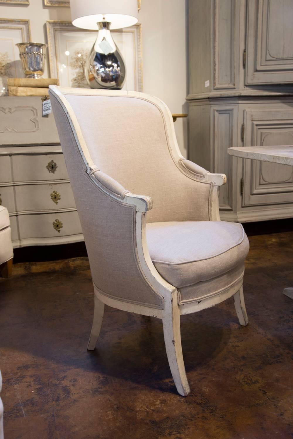 This pair of French painted wood barrel back wing chairs from the 19th century features a new French linen upholstery covering the backs and seats (with added cushion). The scrolled arms are partially upholstered. The barrel backs offer nice comfort