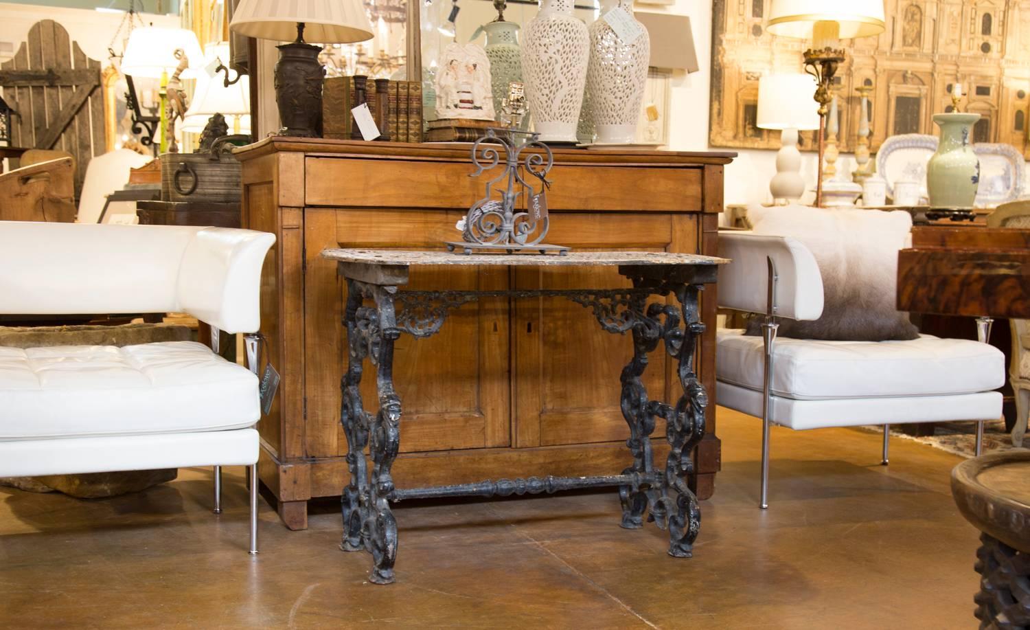 This French wrought iron table from the early 20th century features a painted pierced top decorated with a myriad of cruciform motifs over an intricate base. This trestle type base is made of two lateral legs connected to one another with a