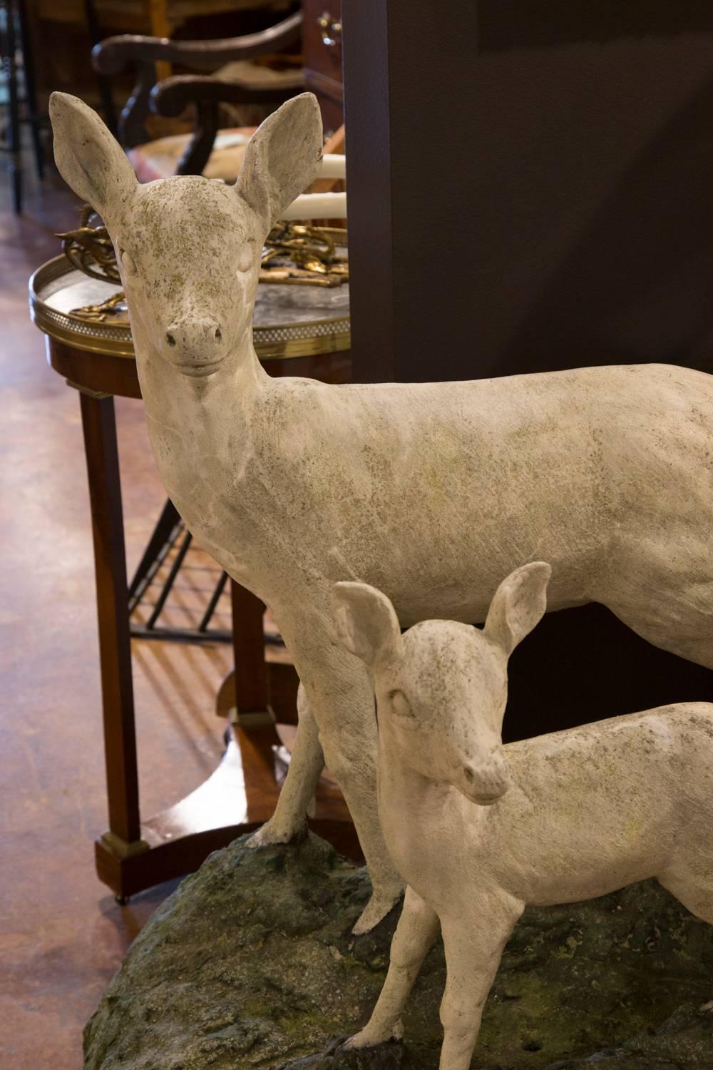 This pair of English cast stone deer sculptures was created in the mid-20th century. Featuring an alert doe with her fawn, both sculptures are placed on a single base depicting the grass on which they are walking. Both animals have raised their
