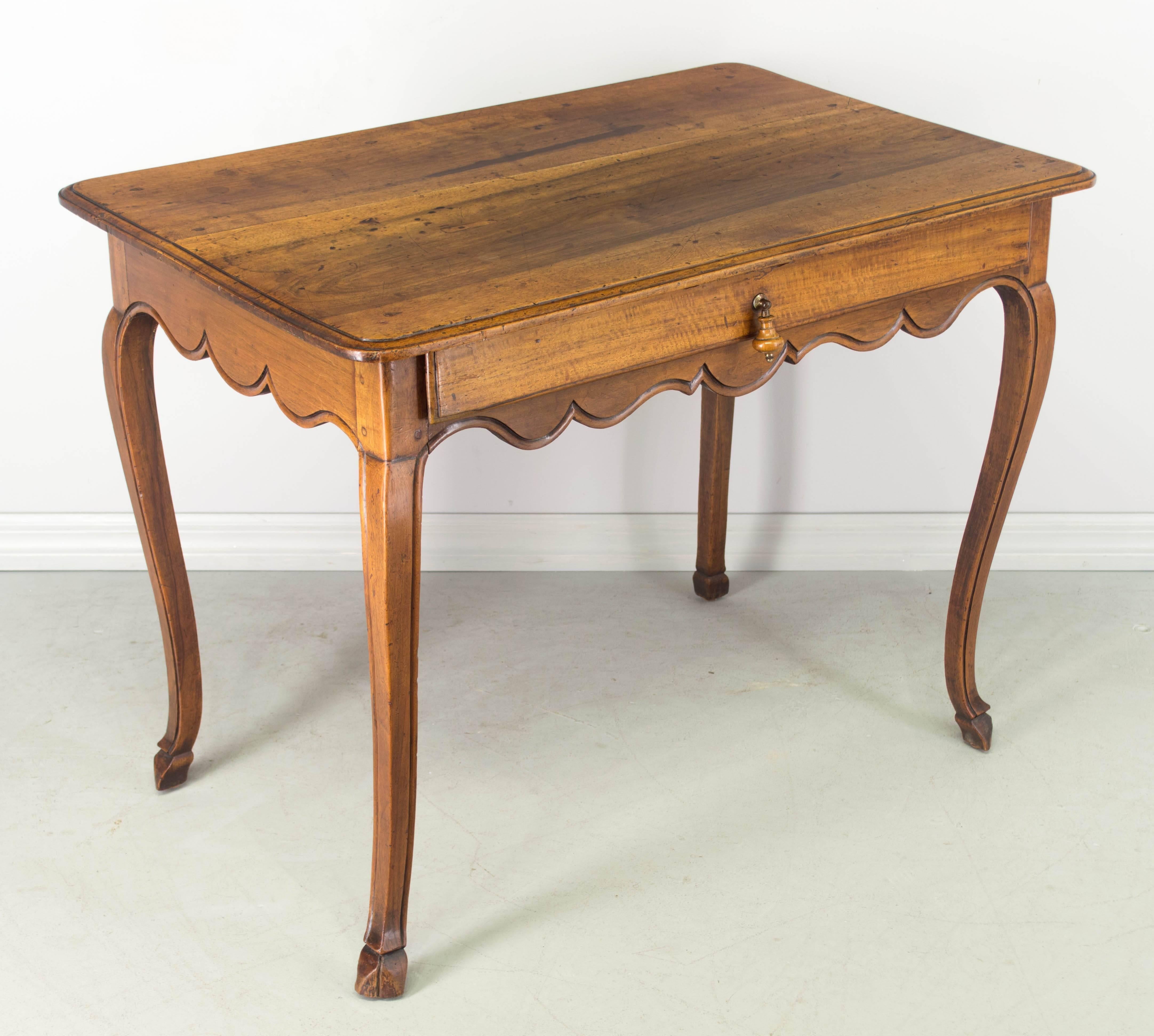 18th century Louis XV side table or desk made of solid walnut with scalloped apron. Single dovetailed drawer with turned wood pull. Nice curved legs with deer hoof feet. Waxed finish. We have a large selection of French antiques. 