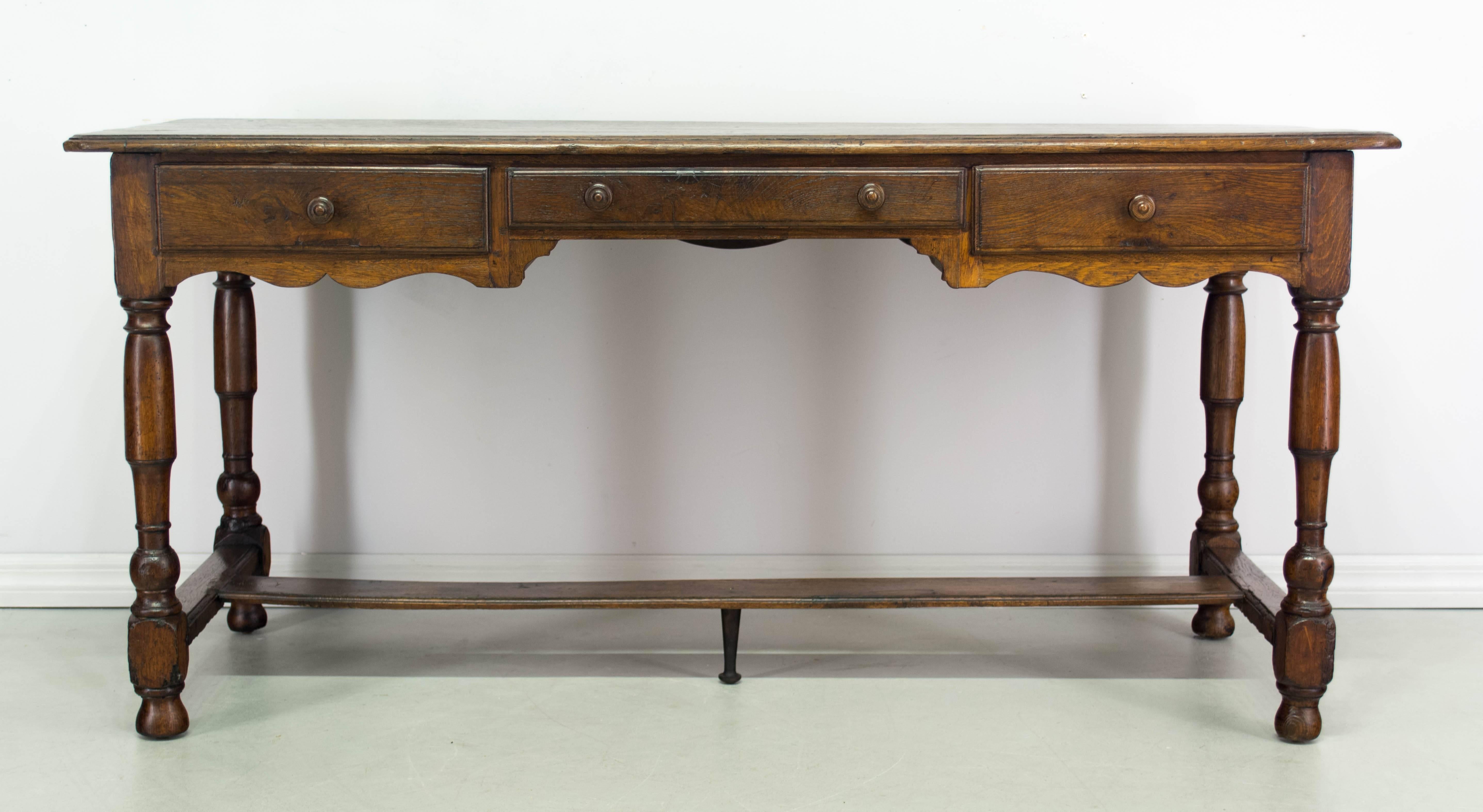 19th century country French bureau plat, or desk made of solid oak with three dovetailed drawers and great writing surface. A sturdy table with turned wood legs and stretcher. Scalloped apron on all four side. A nice size for use as a console,