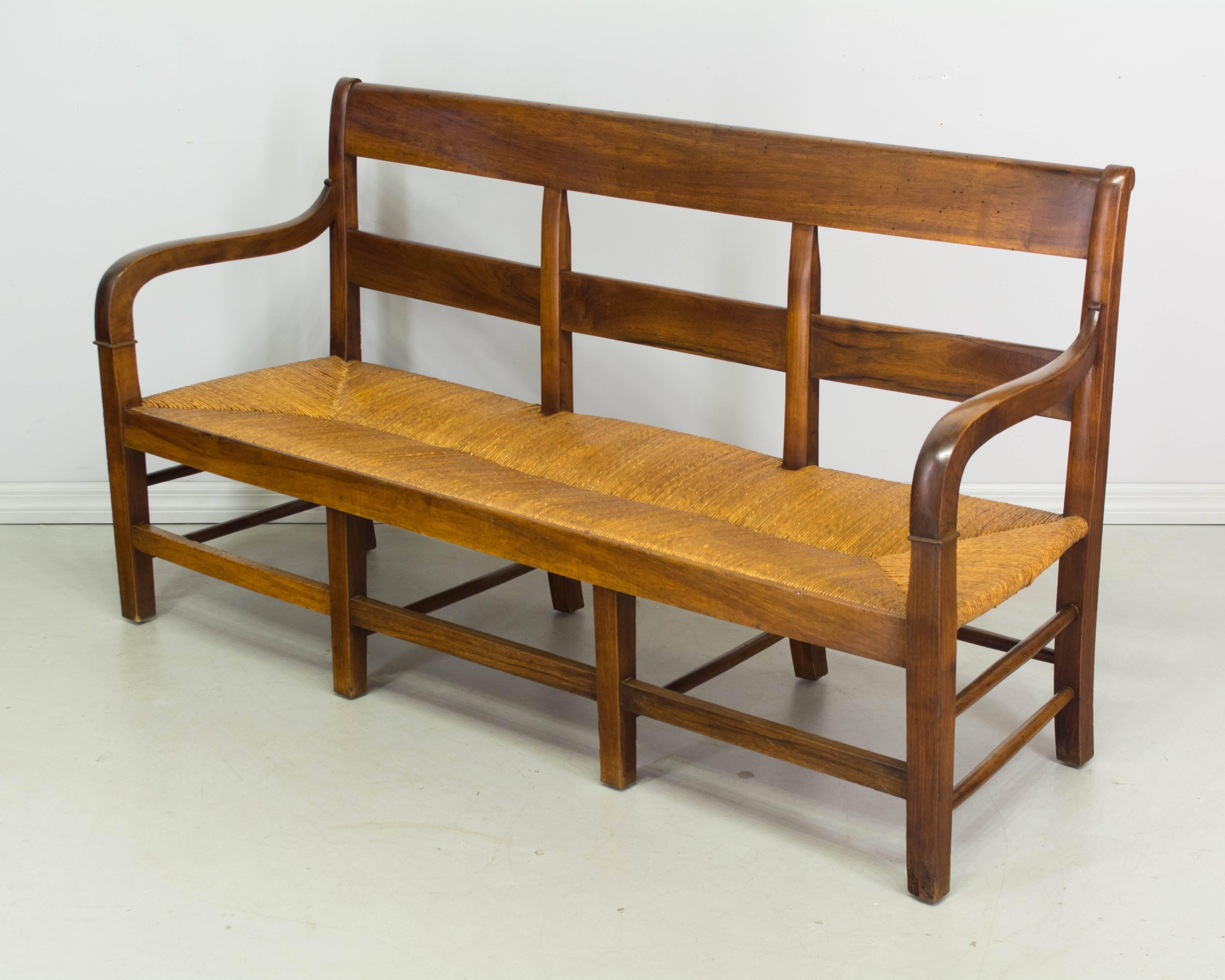 19th century Country French Provençal banquette made of solid walnut with pegged construction. Natural rush seat in excellent condition with old cushion covered in blue plaid linen. Beautiful wood grain with waxed patina. Very sturdy with nice