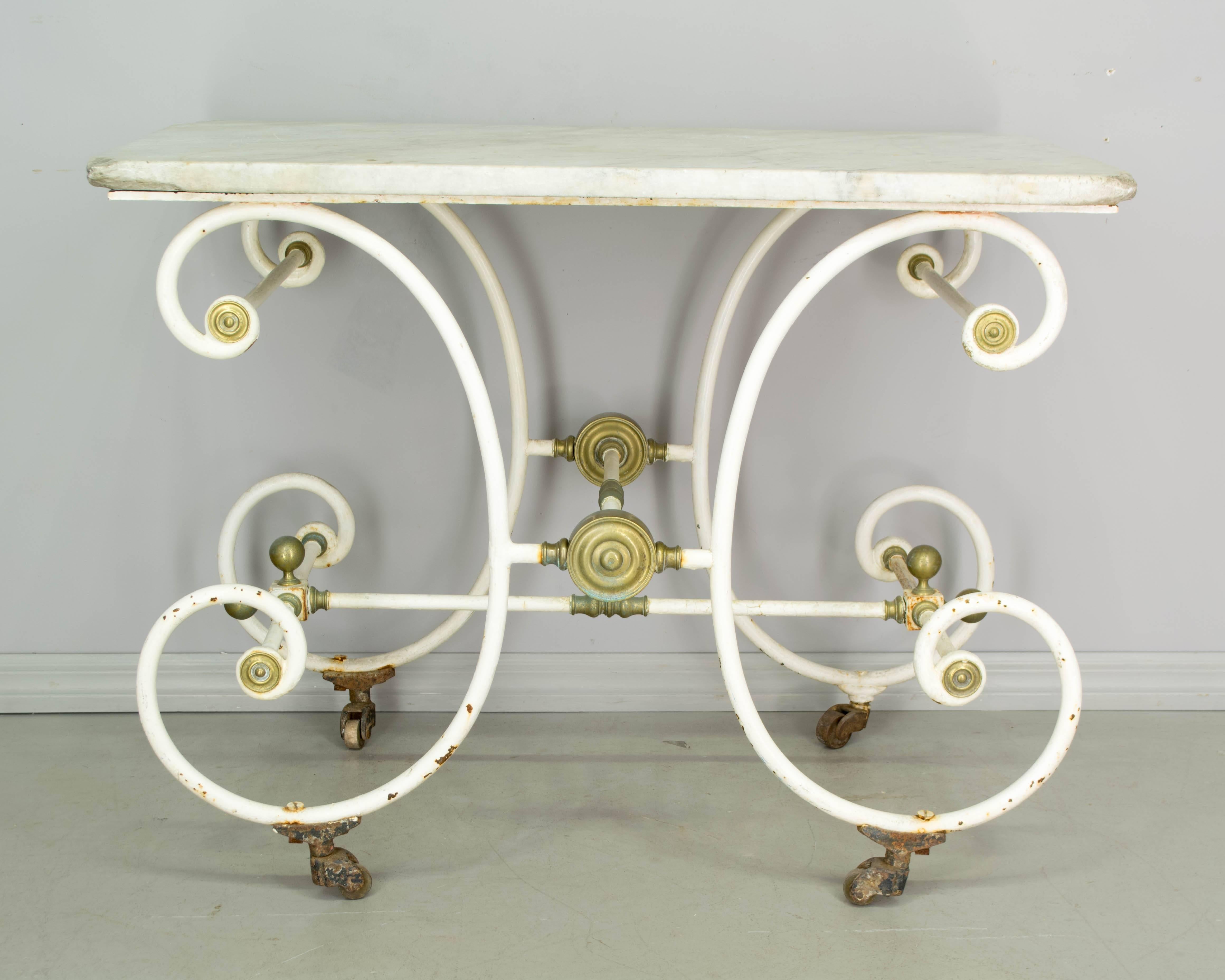 19th century French wrought iron baker's or pastry table with original white painted patina and brass decorative details. Original worn marble top and castors.