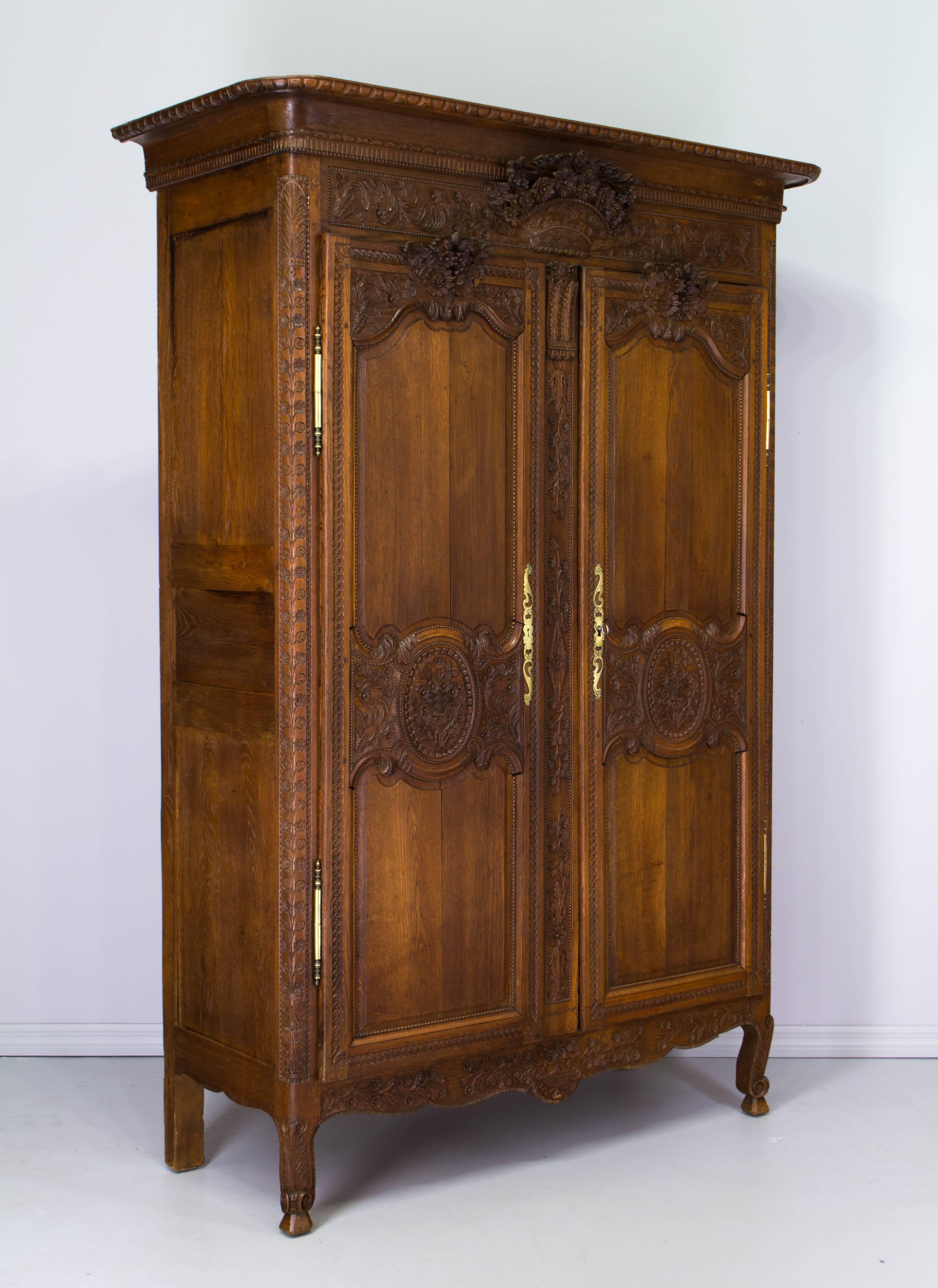 A 19th century Louis XV country French bridal armoire from Normandy. Made of oak with fine hand carving throughout, including a three dimensional flower basket below the crown and floral bouquets above each door. Original brass hardware, with