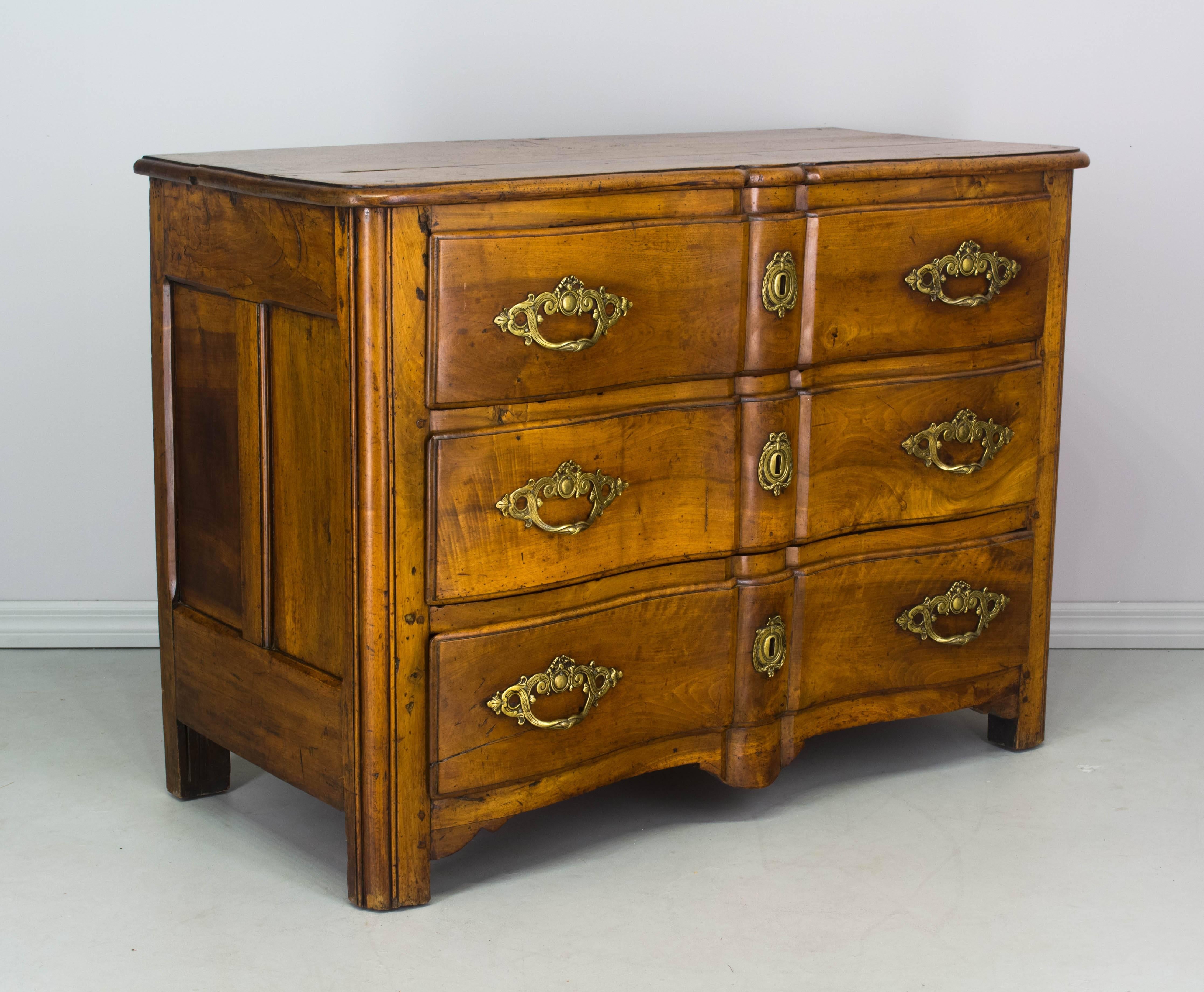 18th century French Regence commode with serpentine front and three dovetailed drawers. Made of solid blonde walnut with beautiful wood grain. Waxed finish. Original bronze hardware, no key. Restoration on top corner of one drawer. The back of one