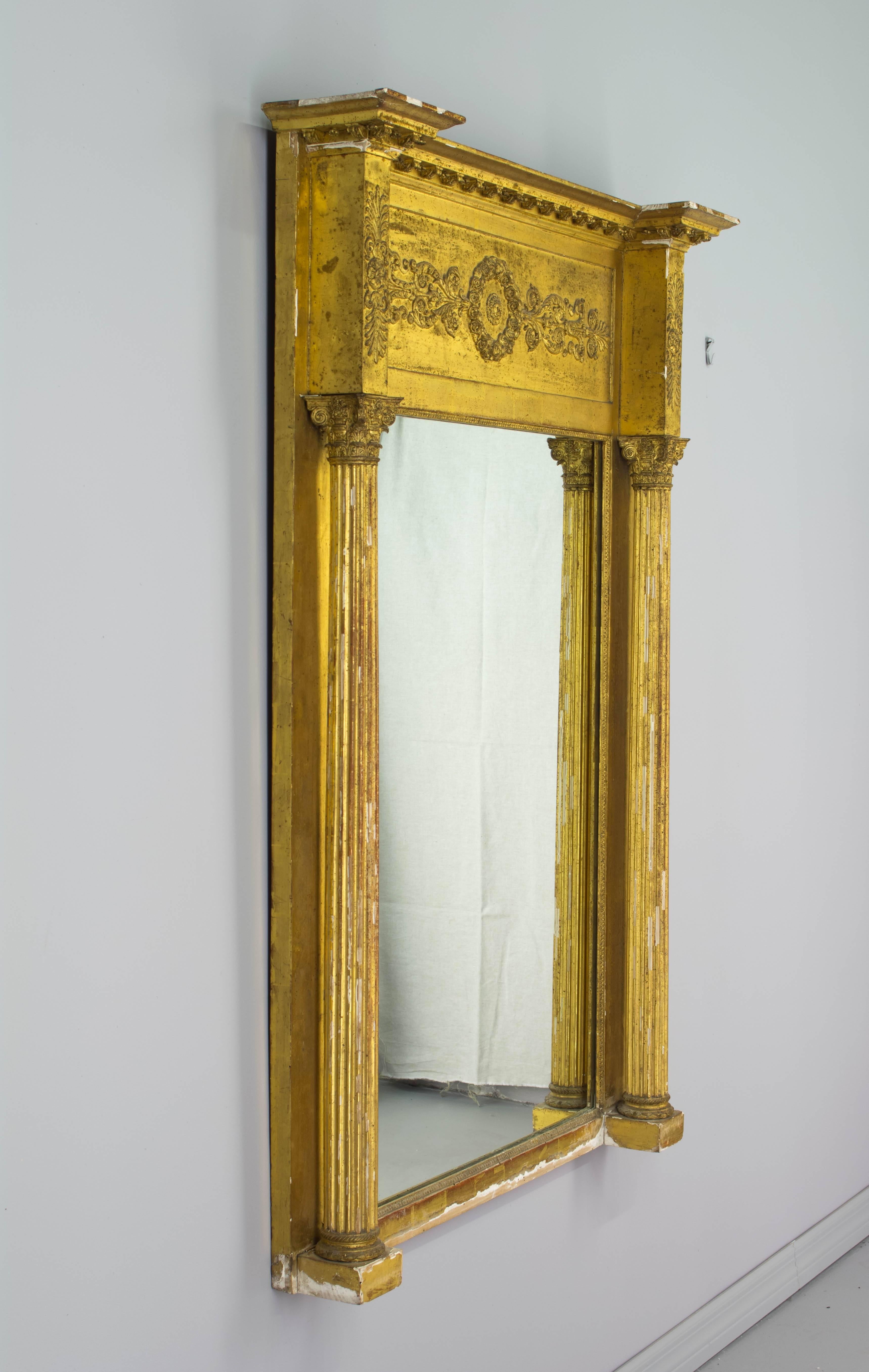 19th century French Empire style gilded mirror. Architectural frame with three dimensional Corinthian columns, a frieze decorated in low relief and capped with a dentil molding. Original mirror. Original gilt is bright, but there are losses