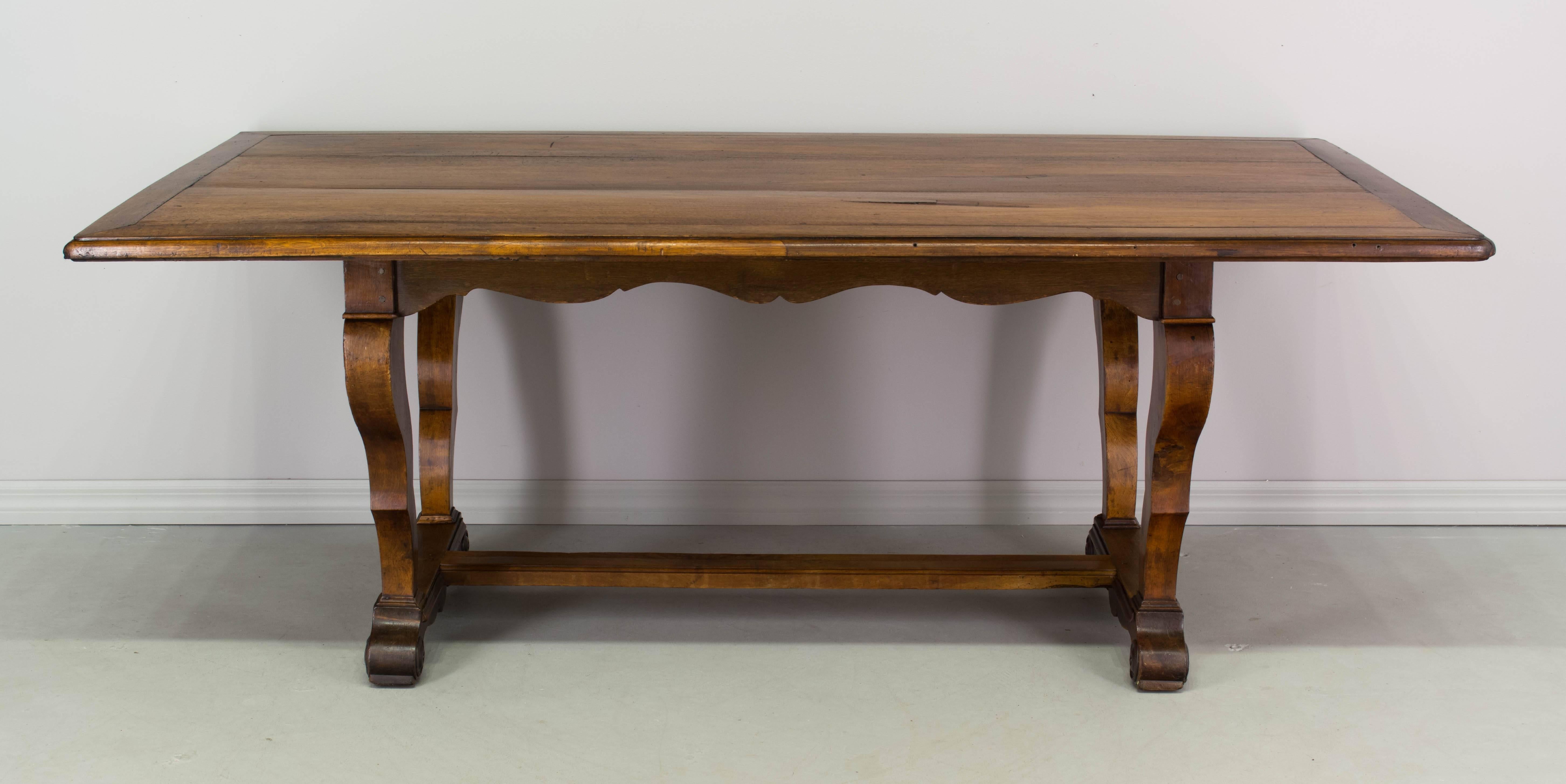 19th century Country French dining table made of solid walnut. The top is made of three planks surrounded with a border and may be removed for shipping purposes.
The base is very sturdy, with sculptural curved legs, a scalloped apron and a central