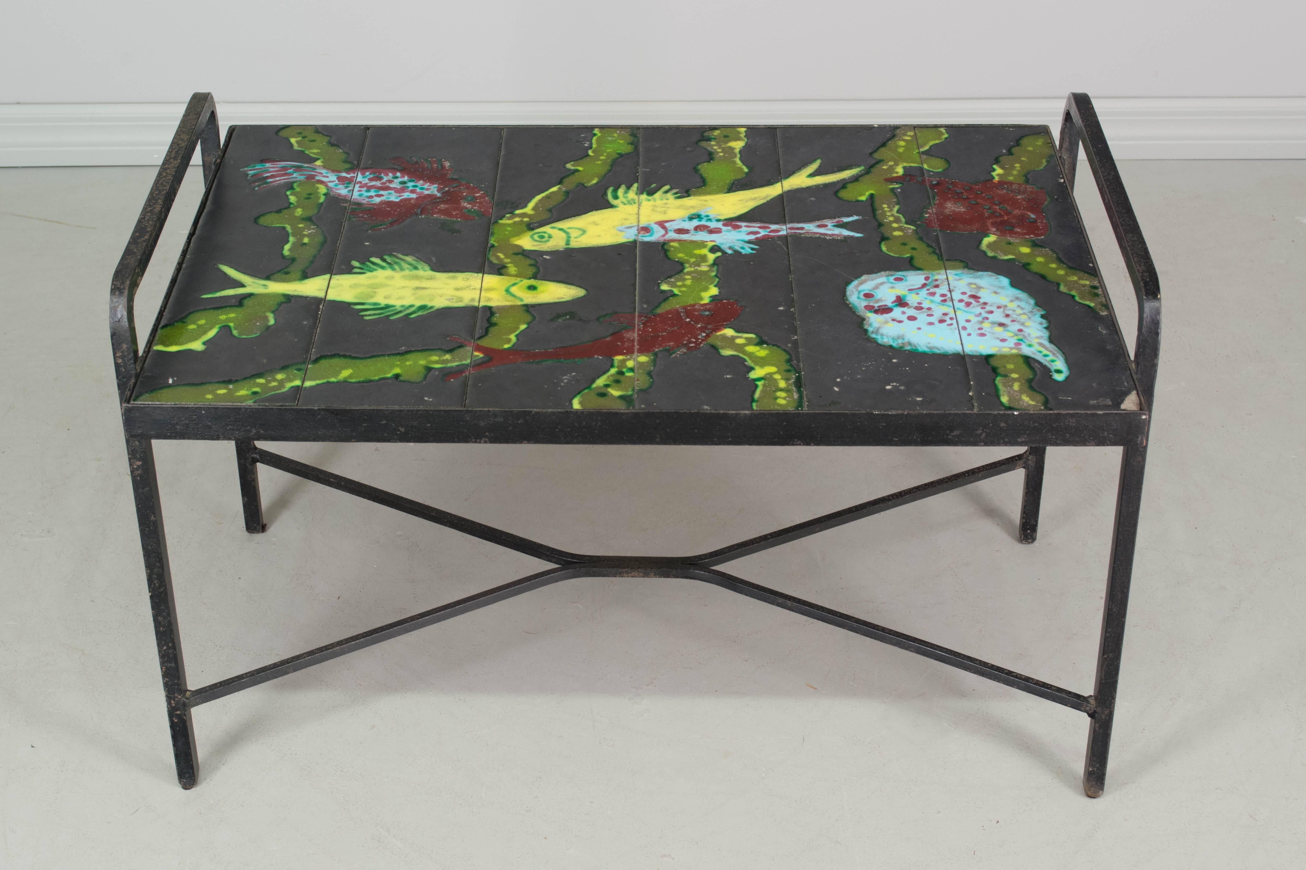 Whimsical French Mid-Century Modern tile-top table with colorful enameled fish, attributed to Jacques Adnet. Top is comprised of six lava stone tiles that fit into a black painted iron base. Color is vibrant, but there are some cracks in the enamel
