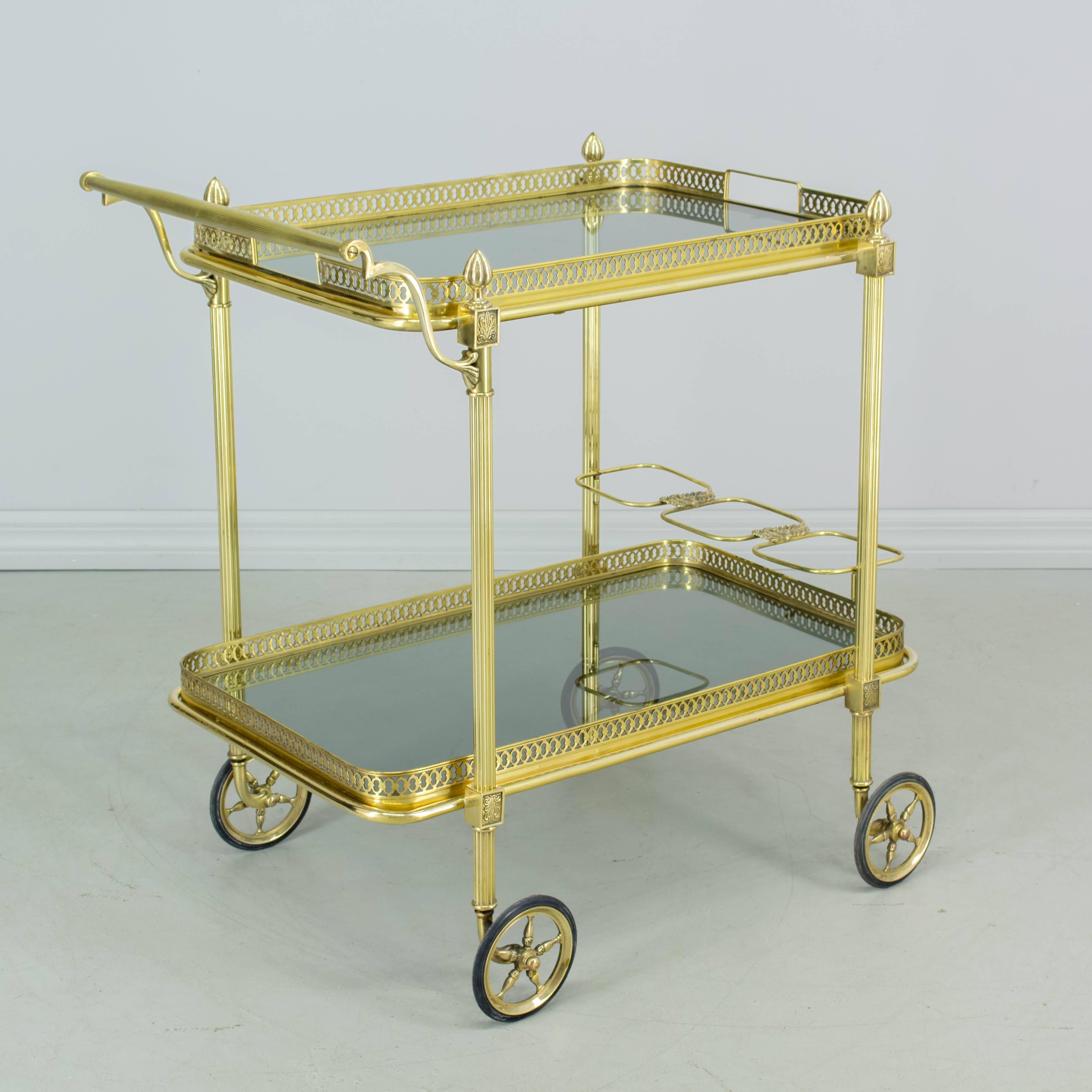 A French bar cart or tea trolley of very fine quality made of brass with smoke glass. Both top and bottom trays remove for serving. Removable bottle rack with decorative detail holds three bottles. Wheels are in excellent condition and glide