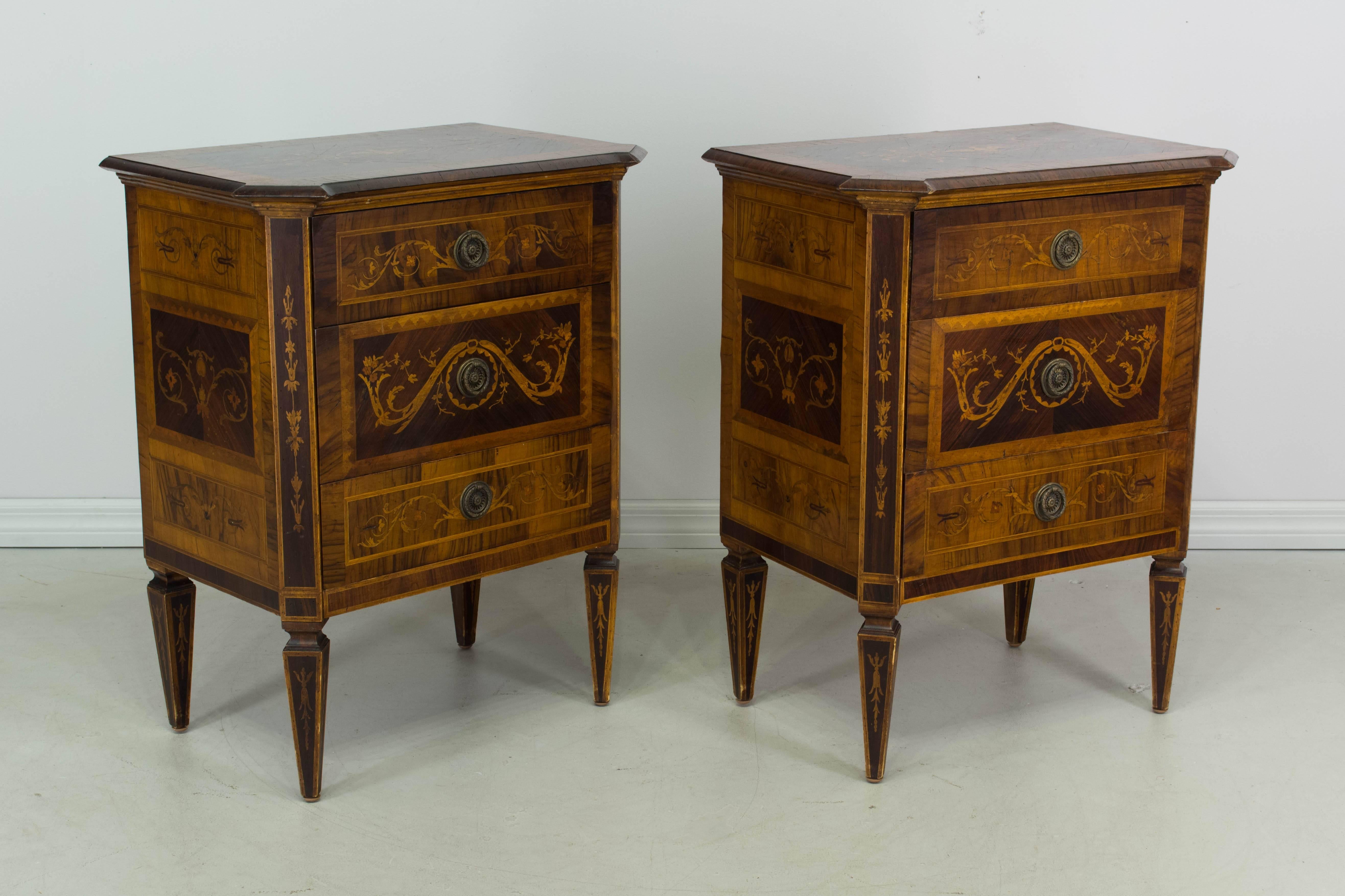 A pair of Italian marquetry commodes or chests of drawers made of walnut with the top, front and sides inlaid with various exotic woods with foliate motifs. Three drawers with original ring pulls. Neoclassical squared and tapering legs. All original