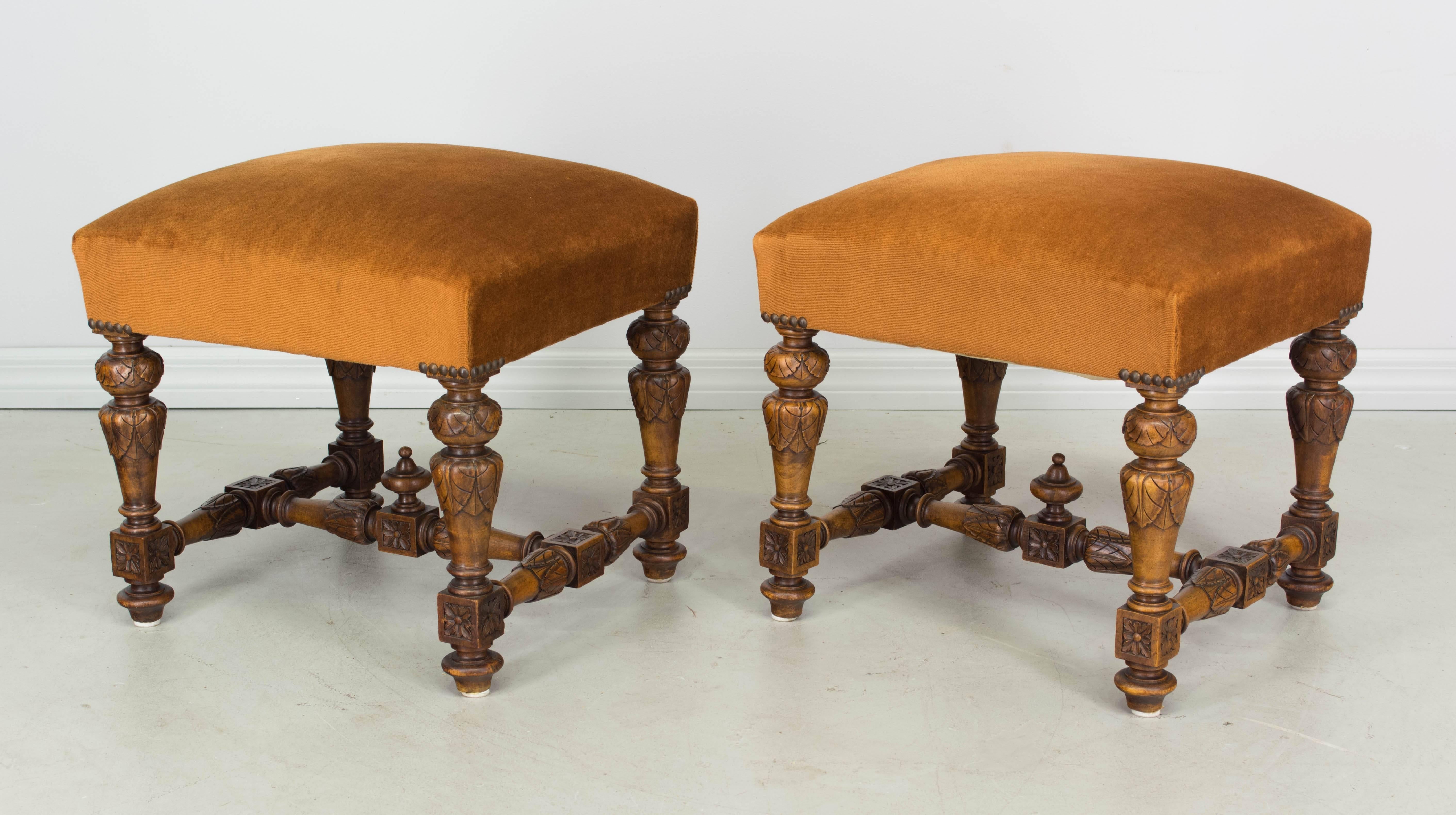 Pair of small French Louis III style stools made of solid walnut. Turned wood legs with carved details and finial in center of stretcher. Very well-made and sturdy. Old velvet upholstery is in serviceable condition.