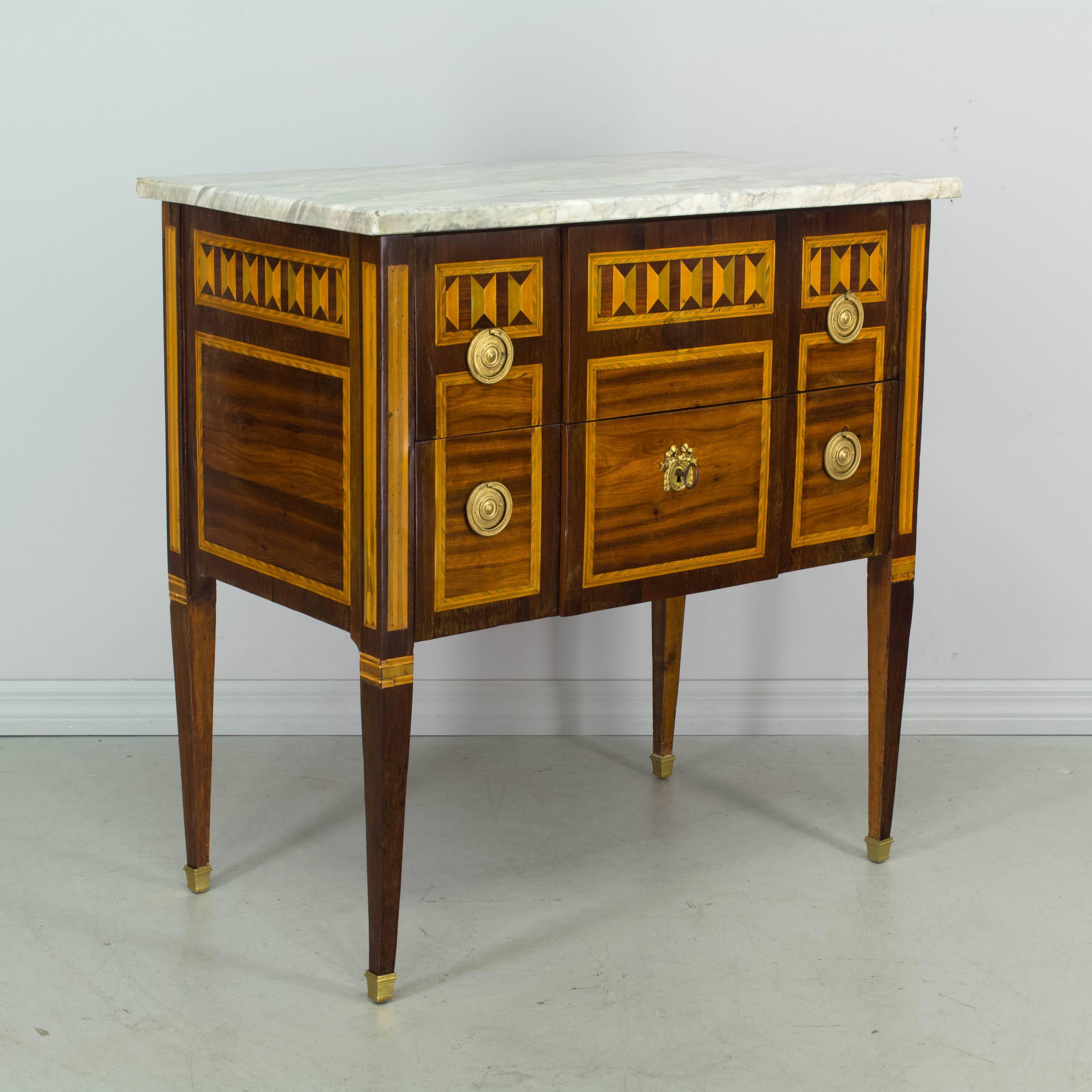 18th century Louis XVI marquetry commode inlaid with veneers of mahogany, walnut and tulip woods. Two dovetailed drawers on slim legs ending in bronze sabots. Original marble-top. Pine as a secondary wood. Original hardware and one lock with a key