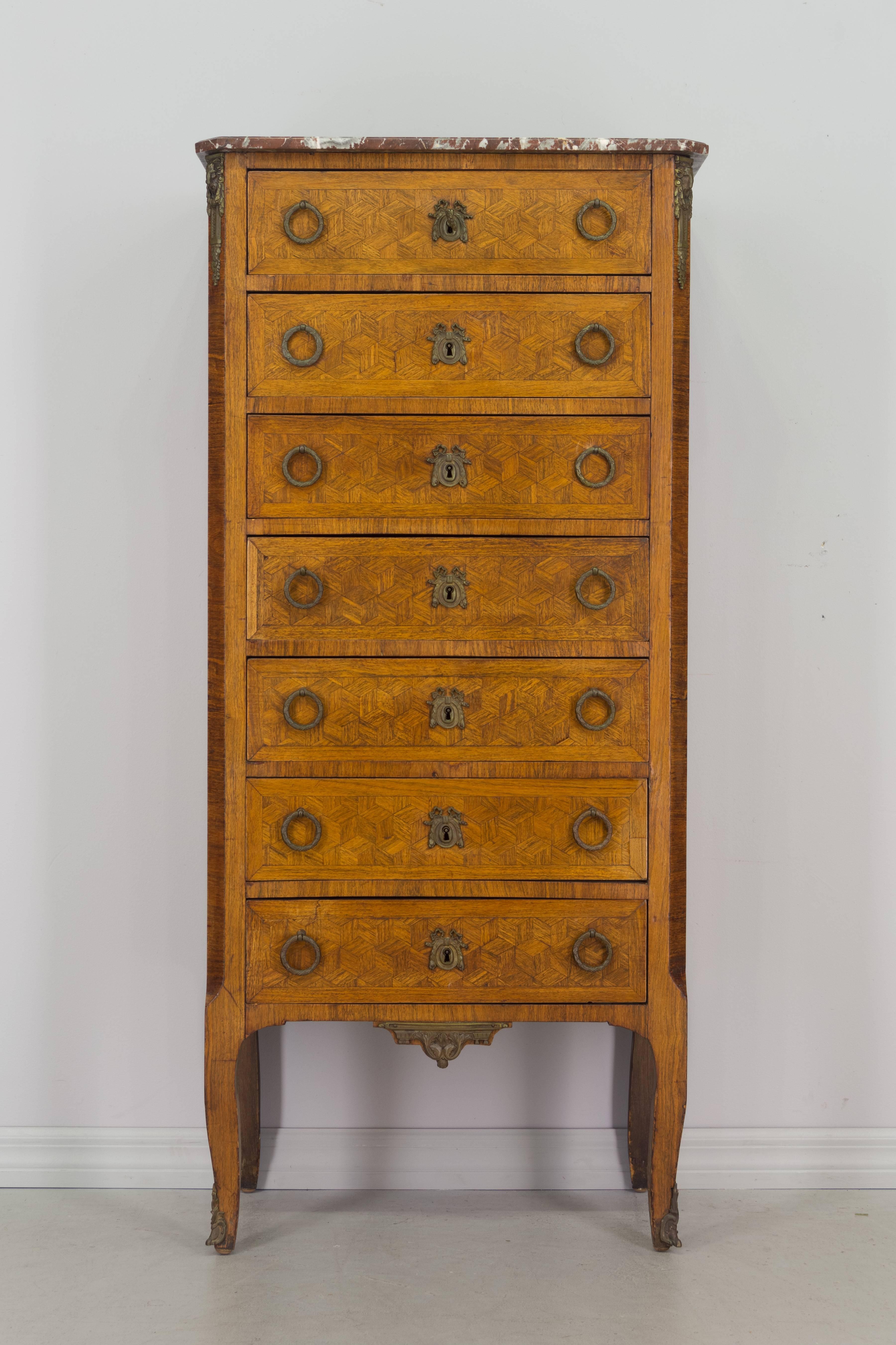 French Louis XVI style semainier or tall chest of seven drawers, made of inlaid veneer of mahogany and walnut with bronze hardware and marble top. All original. Minor veneer losses.