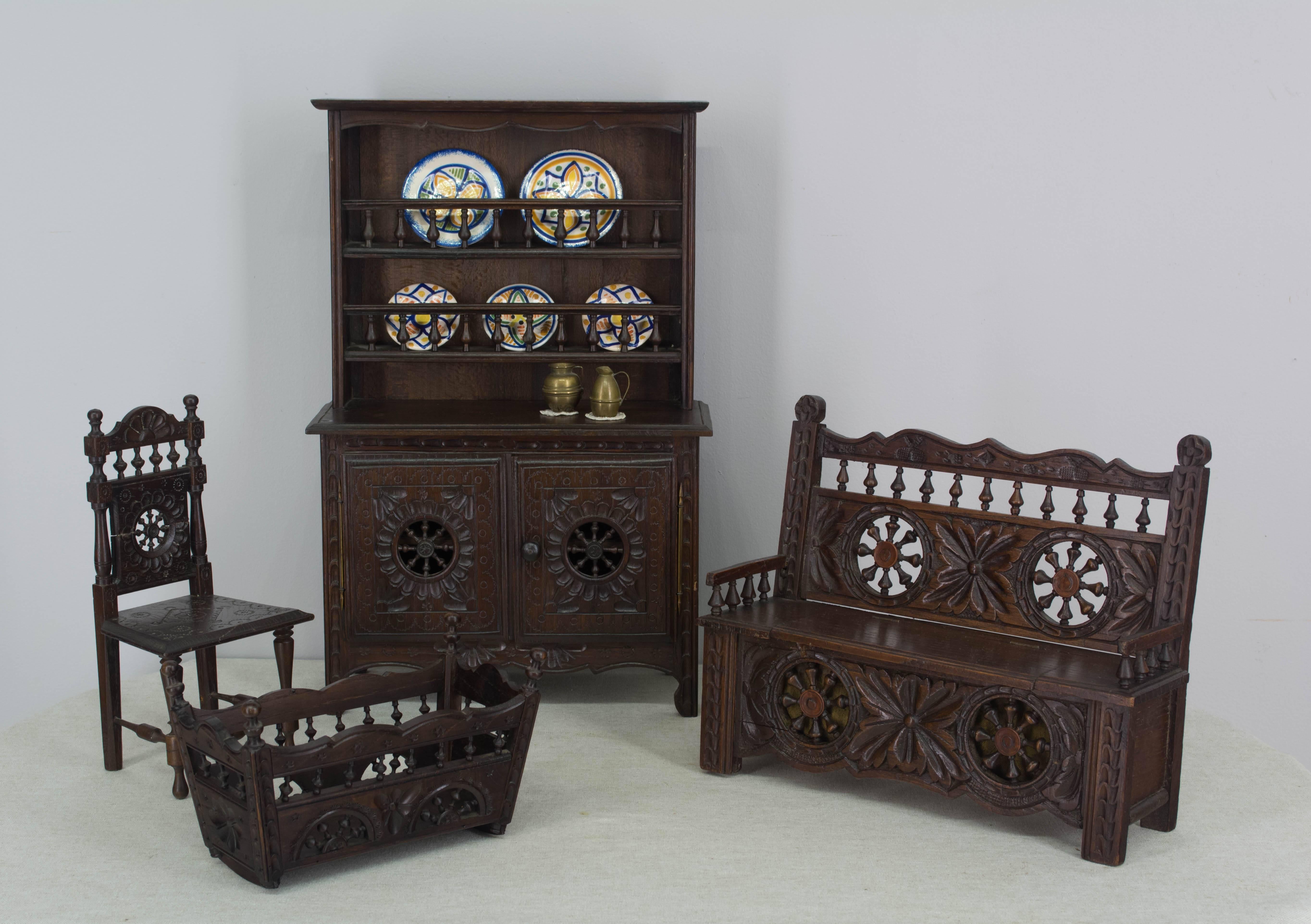 A collection of French miniature doll furniture and accessories from Brittany, made of oak with hand-carved decorative details Set includes: a buffet with plate rack that has six faience plates and two brass pitchers; a bench with hinged seat, a