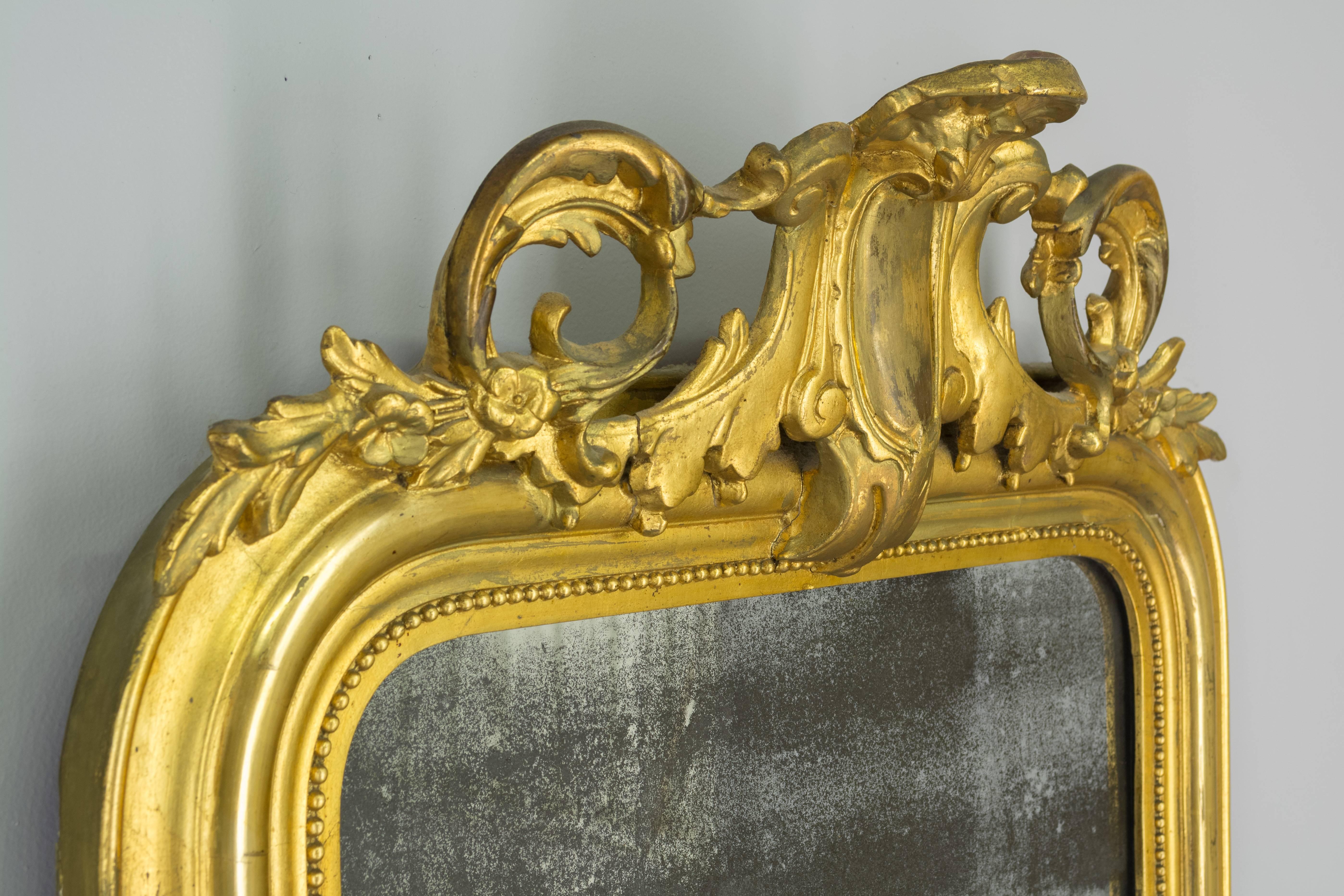 French Louis XV style gilded mirror with carved crest and corner details. Original looking glass with old silvering. Minor restorations to carvings and touch-ups to gilt. 43" H x 26" W x 1.5" D (6" deep at crest).