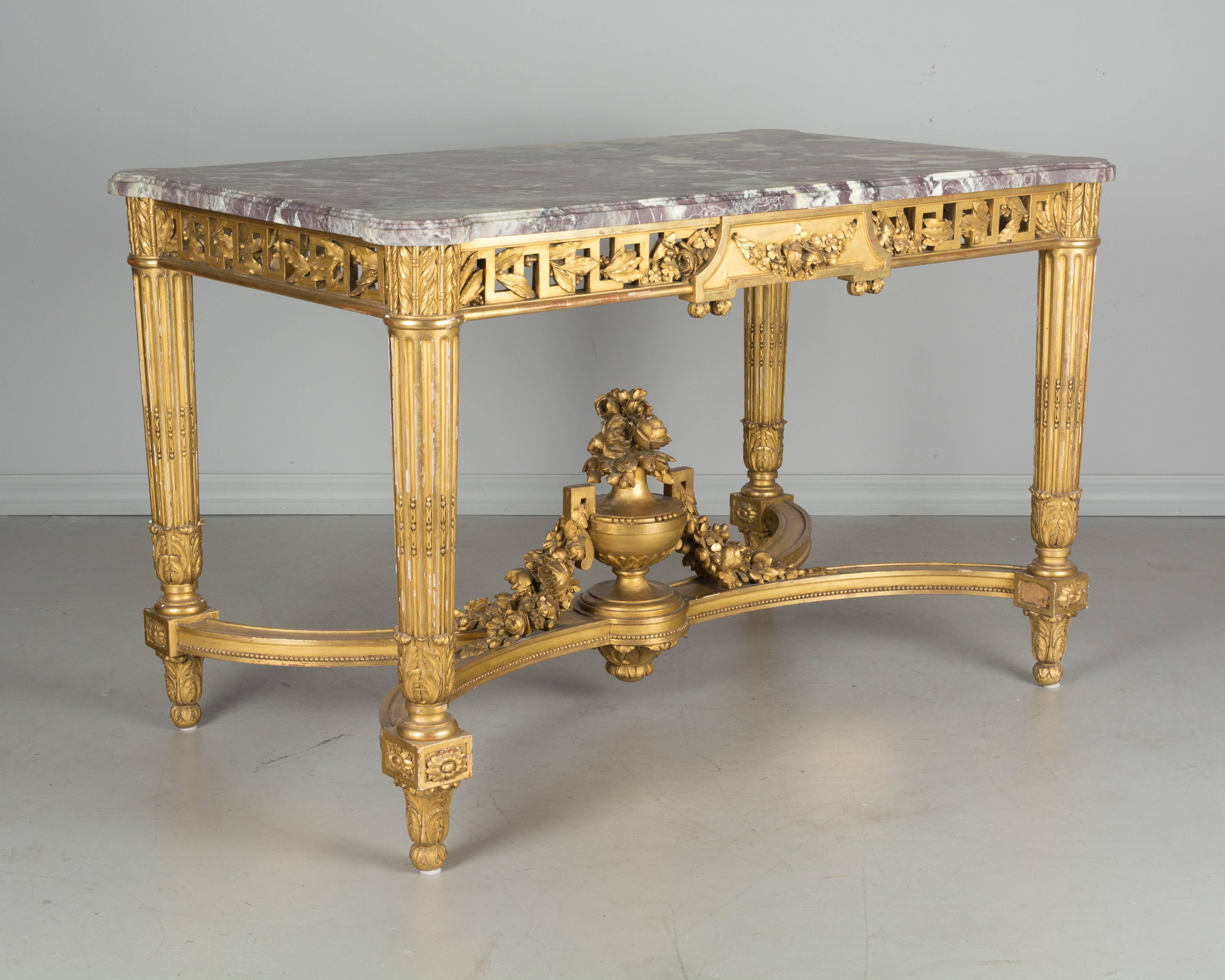19th century Louis XVI style marble top, gilt decorated center table. Fluted legs with center stretcher. Sculptural flower urn with floral garlands. Original marble top with beautiful lavender and grey coloring, shaped corners and grooved edge. Some