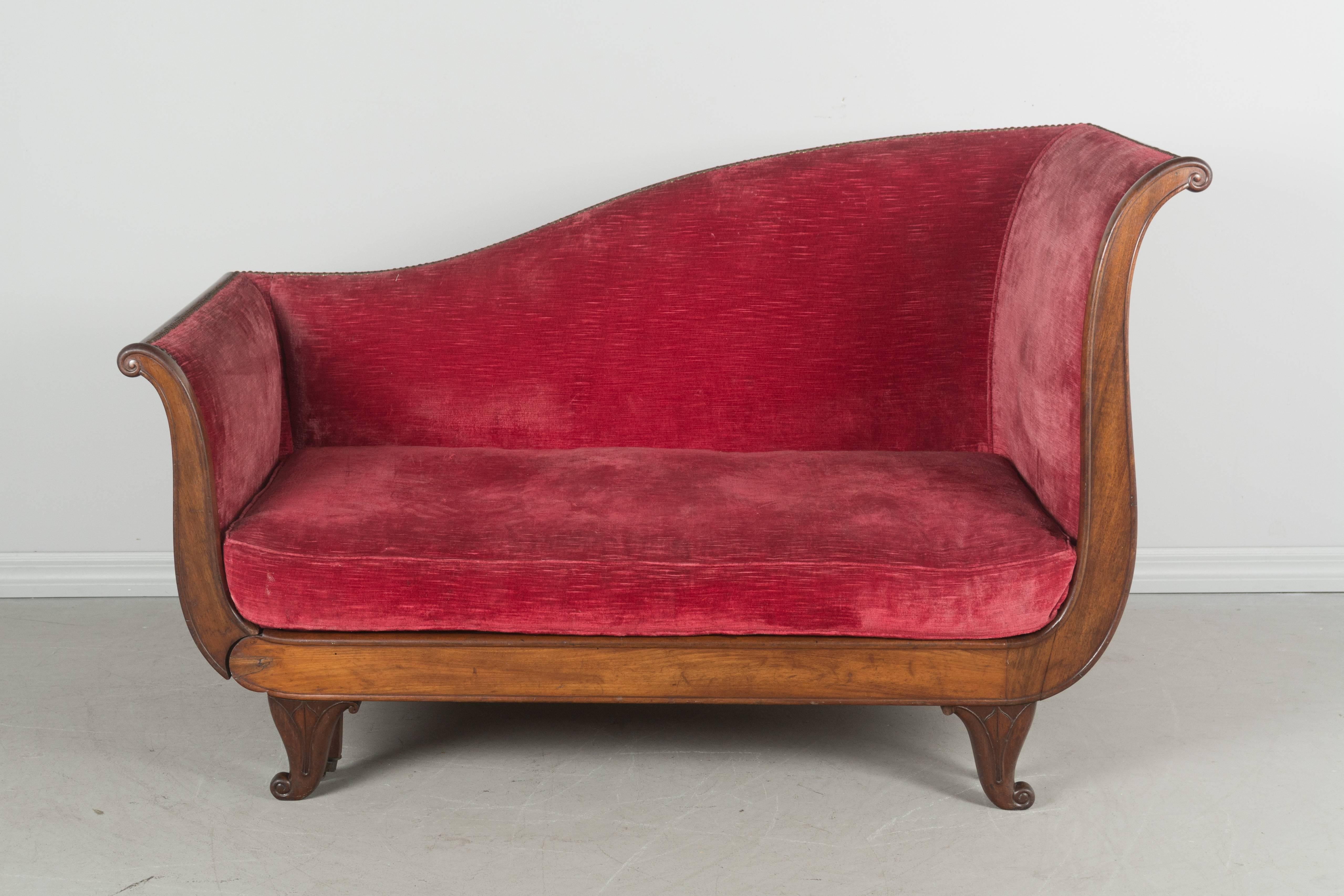 19th century French Empire style méridienne or settee with mahogany frame. One side hinges down to create a daybed, or chaise for reclining. Original castors glide easily. Old velvet upholstery is serviceable. 
Overall: 58" W x 27.5" D x