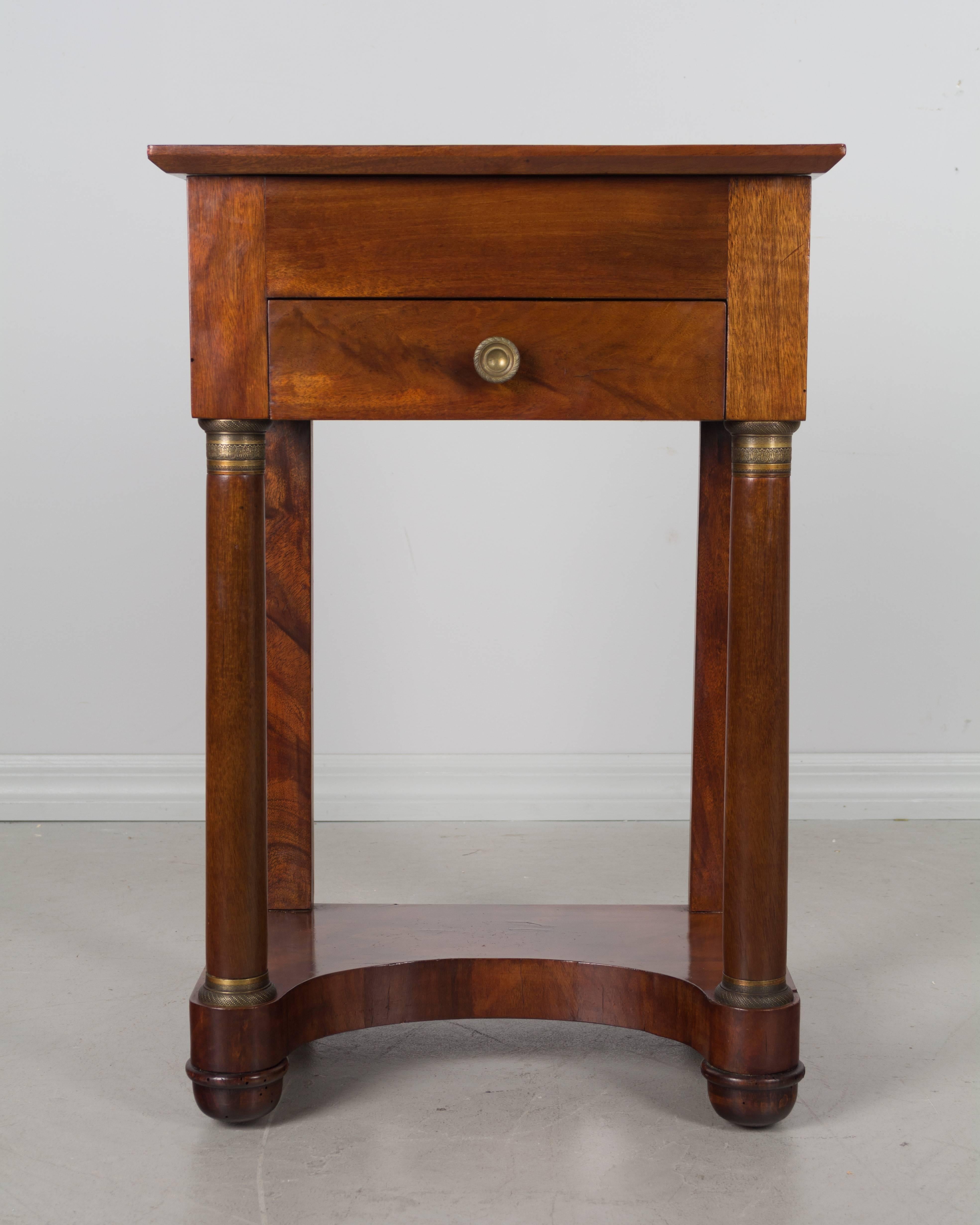 An early 19th century, French empire style mahogany side table or nightstand. Dovetailed drawer beneath a hinged top opening to reveal a mirror and small compartments. Front columns with bronze decoration. French polish finish Old repair to back