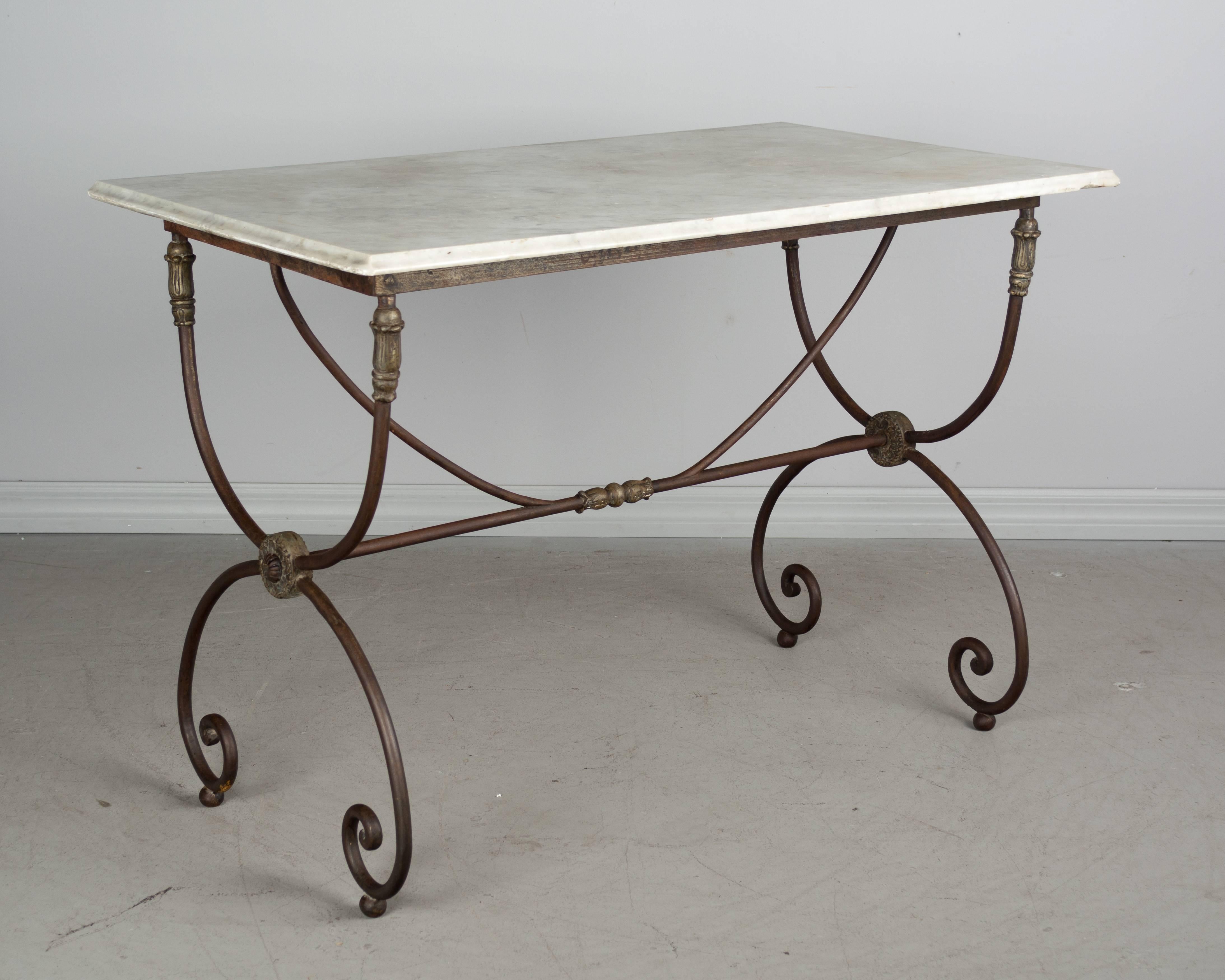 French bistro or pastry table with wrought iron base and original white marble top. Nice warm bronze patina to base with decorative medallions. Hairline in marble, but no structural damage. Marble is edged on three sides.