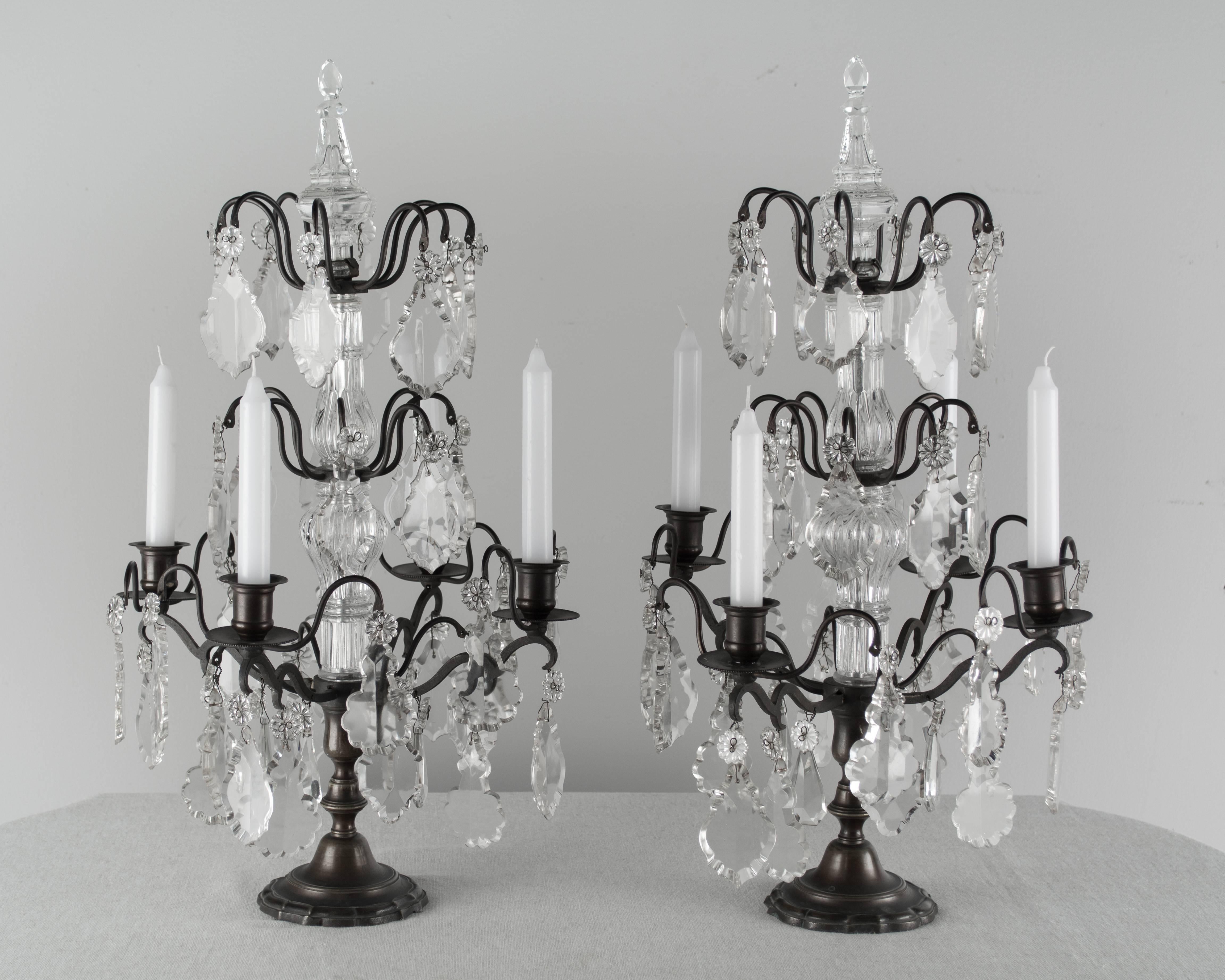 Pair of Louis XV style four-light French girandoles made of brass with antique bronze patina. Three tiers of crystal prisms of various shapes and sizes, crystal columns and finials. Tall, elegant proportions. These have not been rewired and are