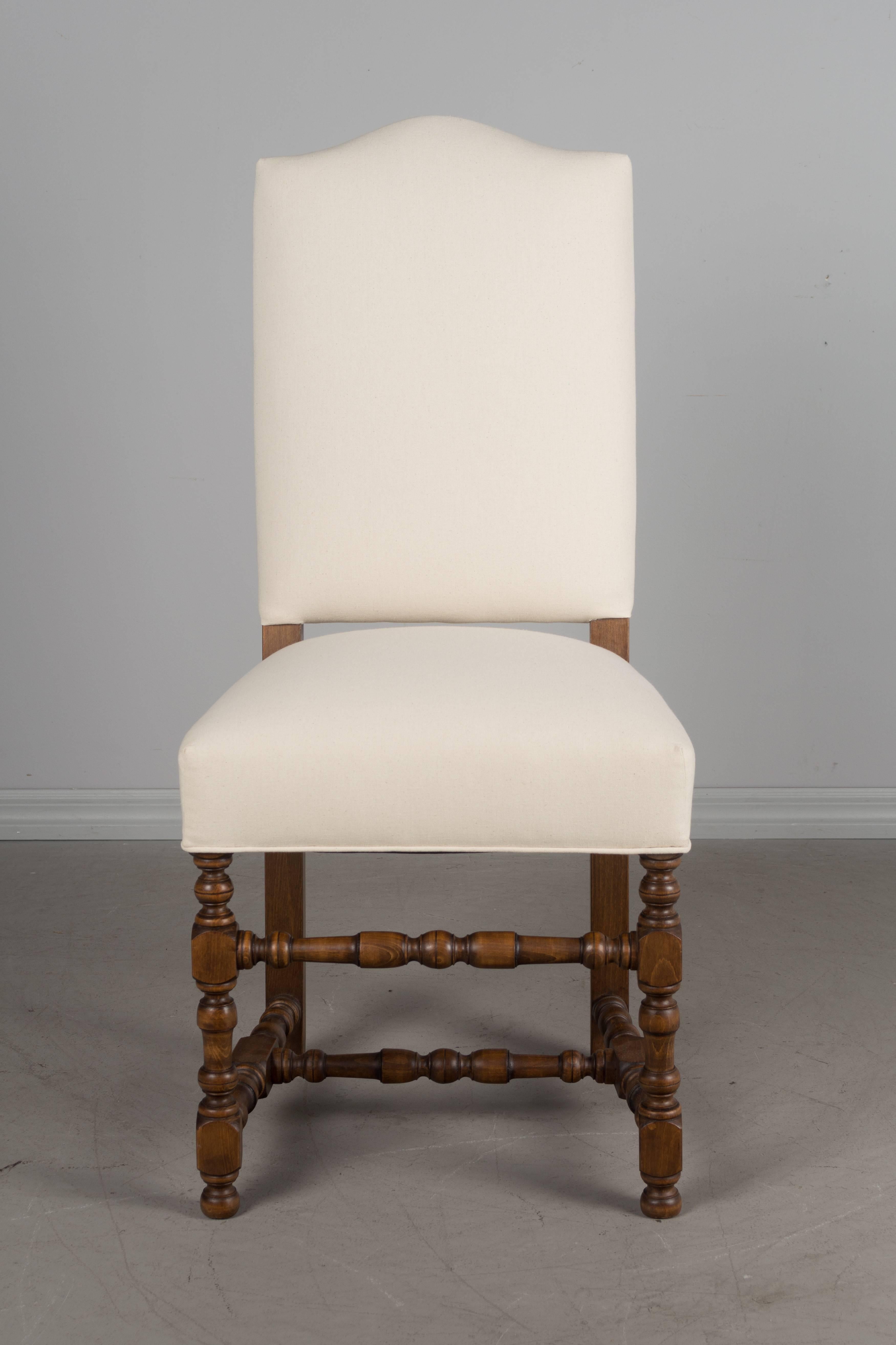 Set of eight elegant French Louis XIII style dining chairs made of beechwood with graceful camelback, turned wood legs and stretcher. Newly reupholstered in natural canvas fabric. Sturdy and comfortable seating.