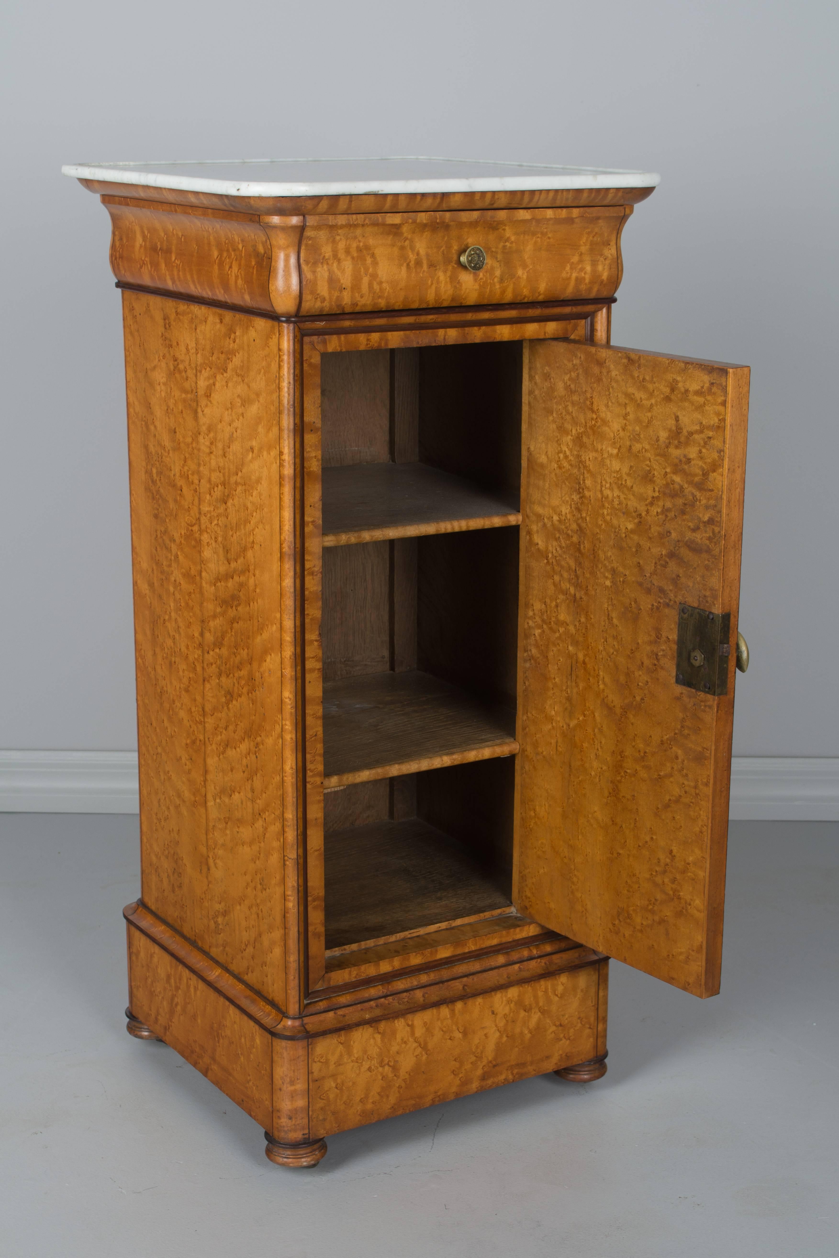 19th century French Charles X-side table or nightstand, made of veneer of bird's-eye maple over solid oak with mahogany trim. Single dovetailed drawer and cabinet door opening to an interior with two shelves. Turned wood feet with brass castors.