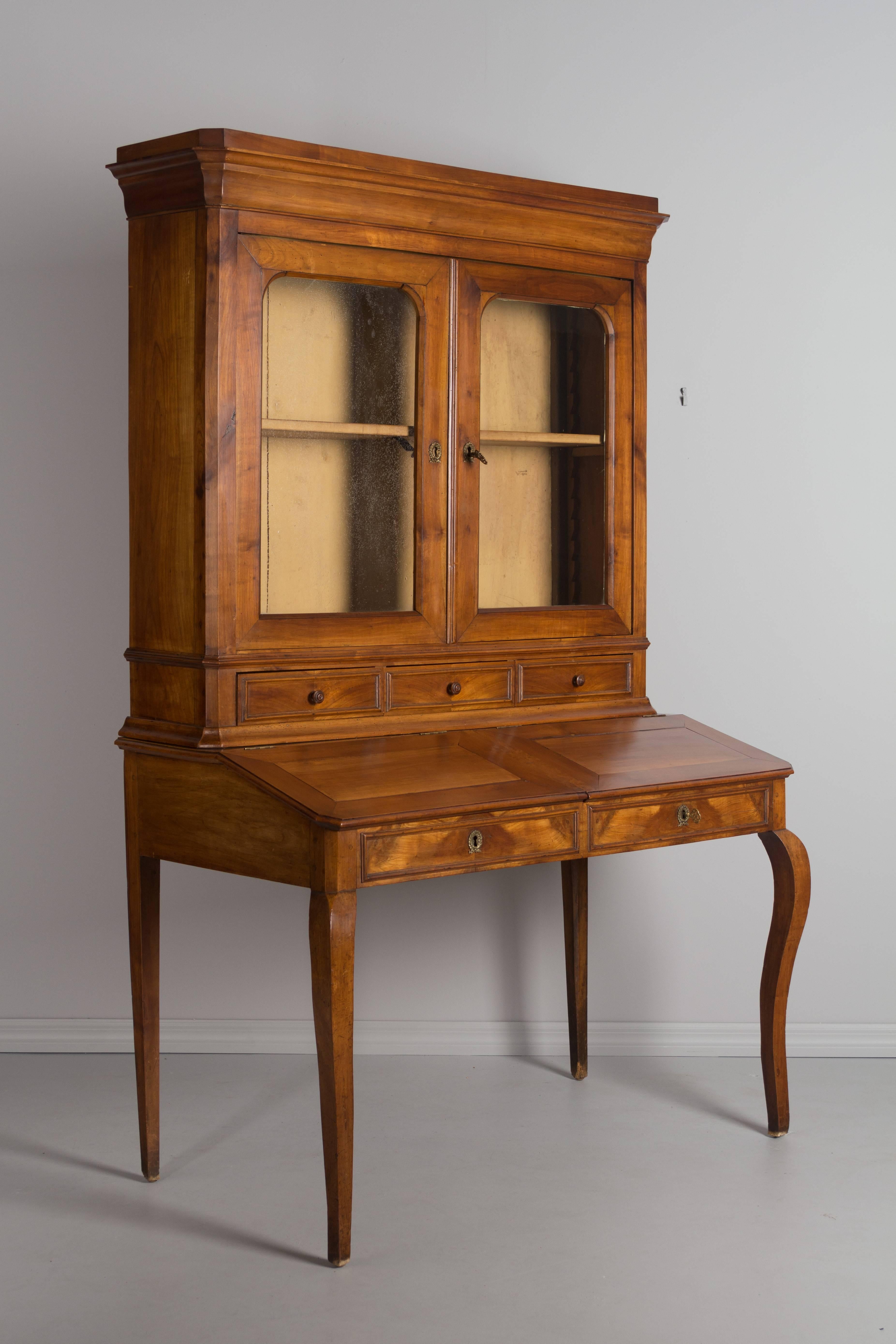 A 19th century Country French slant top desk with bookcase. Made of solid cherry with waxed patina. The top part has original glass paned doors opening to a single adjustable shelf above three dovetailed drawers with turned wood knobs. This desk was