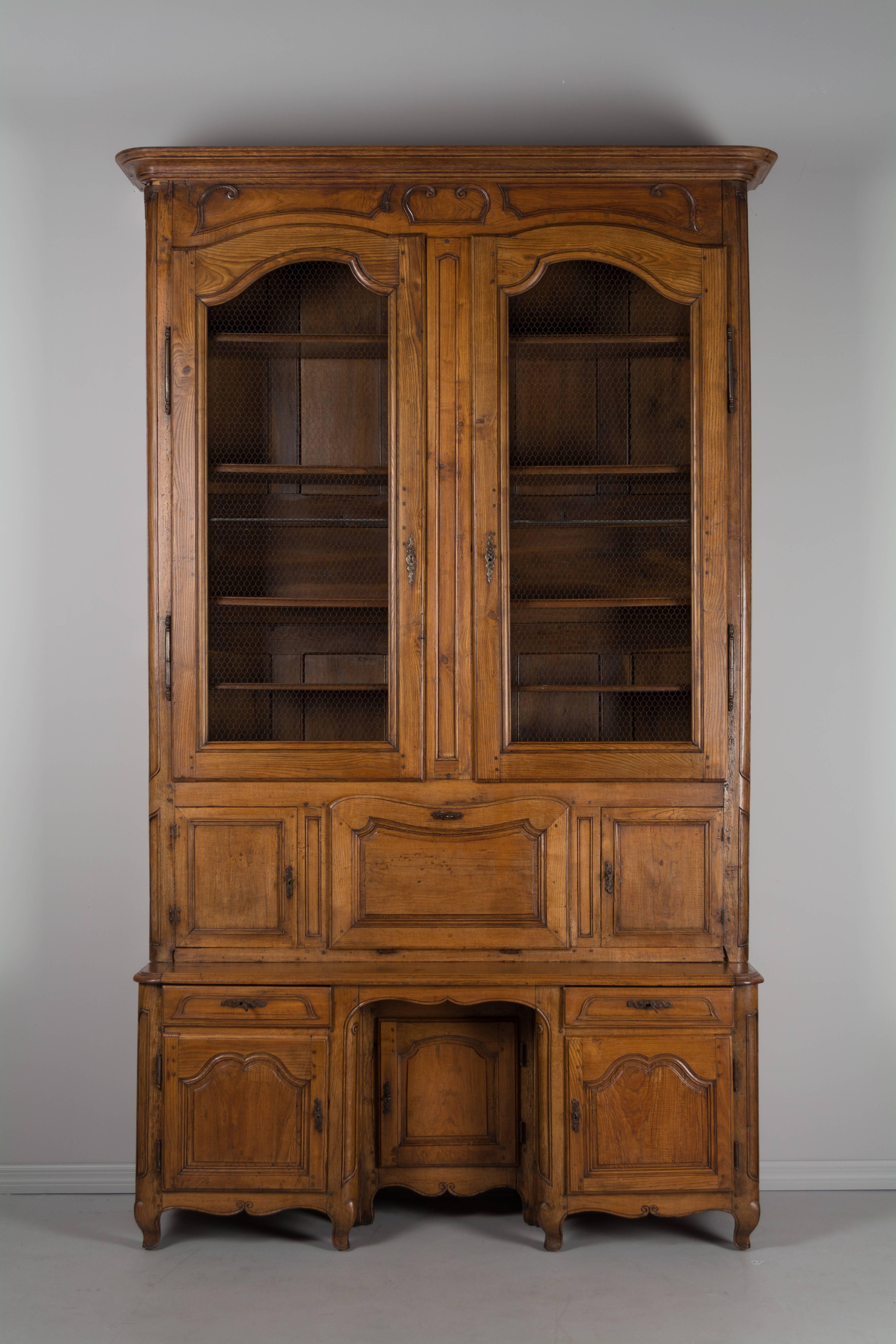 A grand scale 18th century French bibliothèque with scriban, or drop-leaf desk made of solid elmwood. The large bookcase has chicken wire doors opening to four adjustable shelves, above a drop leaf desk flanked by two locking cabinets. The interior