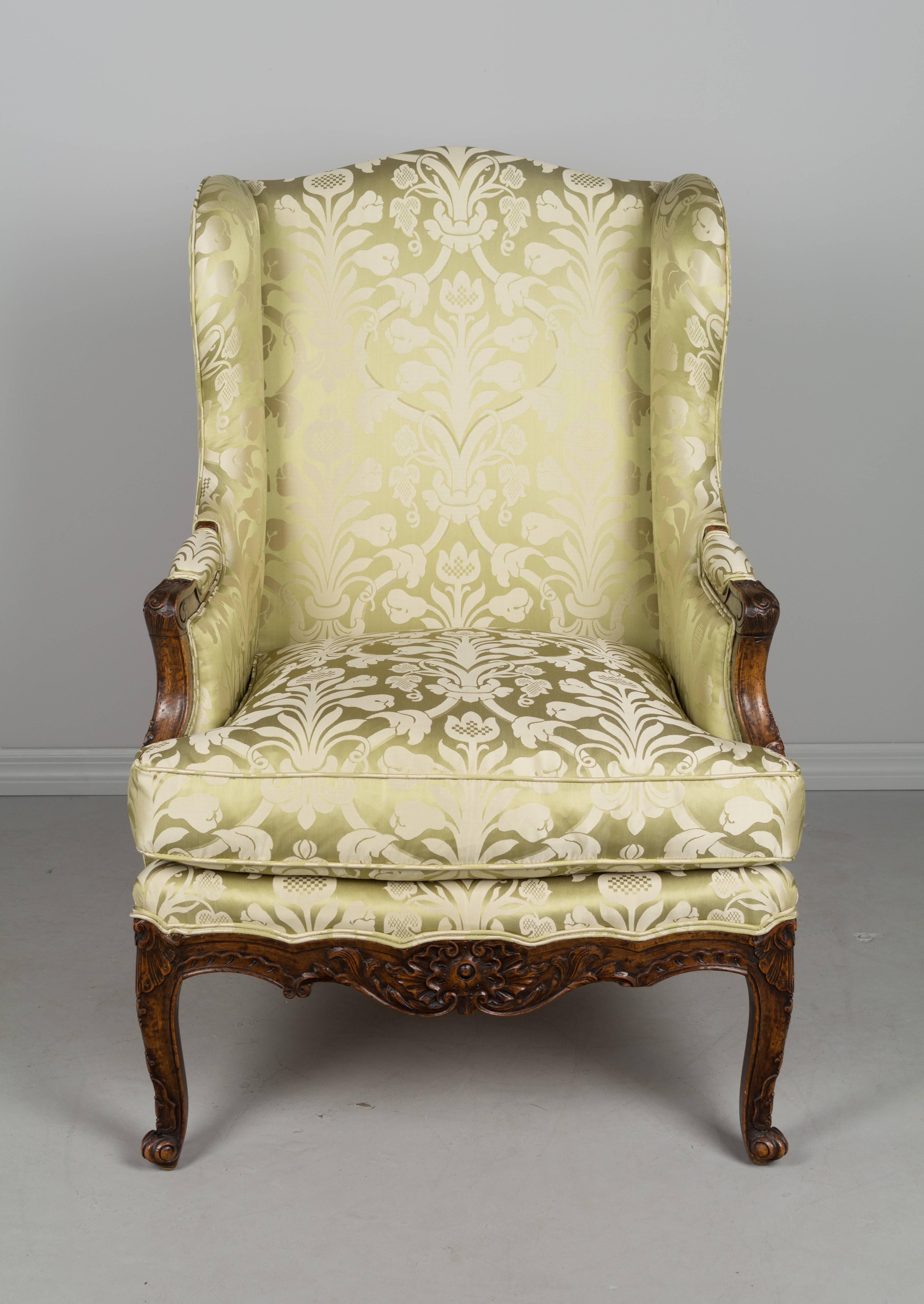 19th century French Louis XV style bergere or wing chair. Walnut frame with hand-carved details. Newly reupholstered in beautiful celery green silk damask fabric. Down seat cushion. A sturdy armchair with comfortable seating. In very good condition