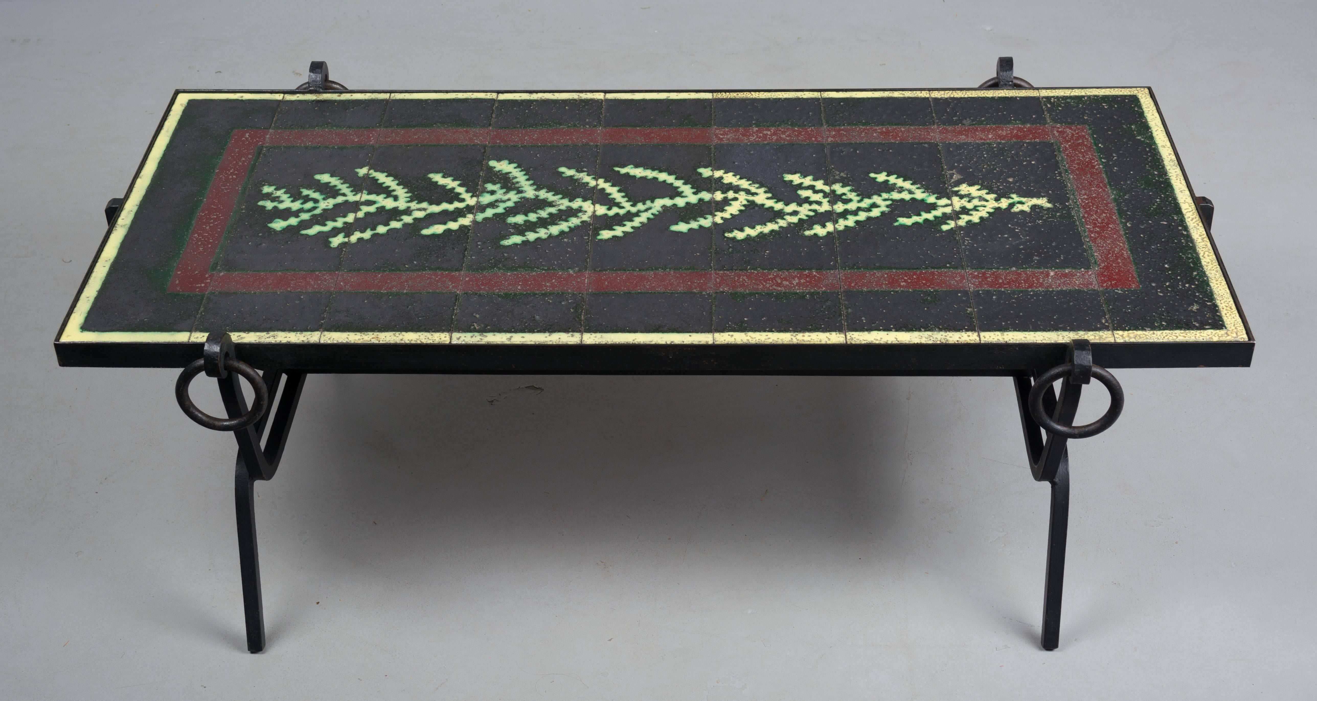 Mid-Century Modern Jacques Adnet wrought iron table with glazed lava stone tile top. Nine tiles form a green vine or seaweed design on a black ground with burgundy border and yellow outline around the perimeter. Tile are in excellent condition with