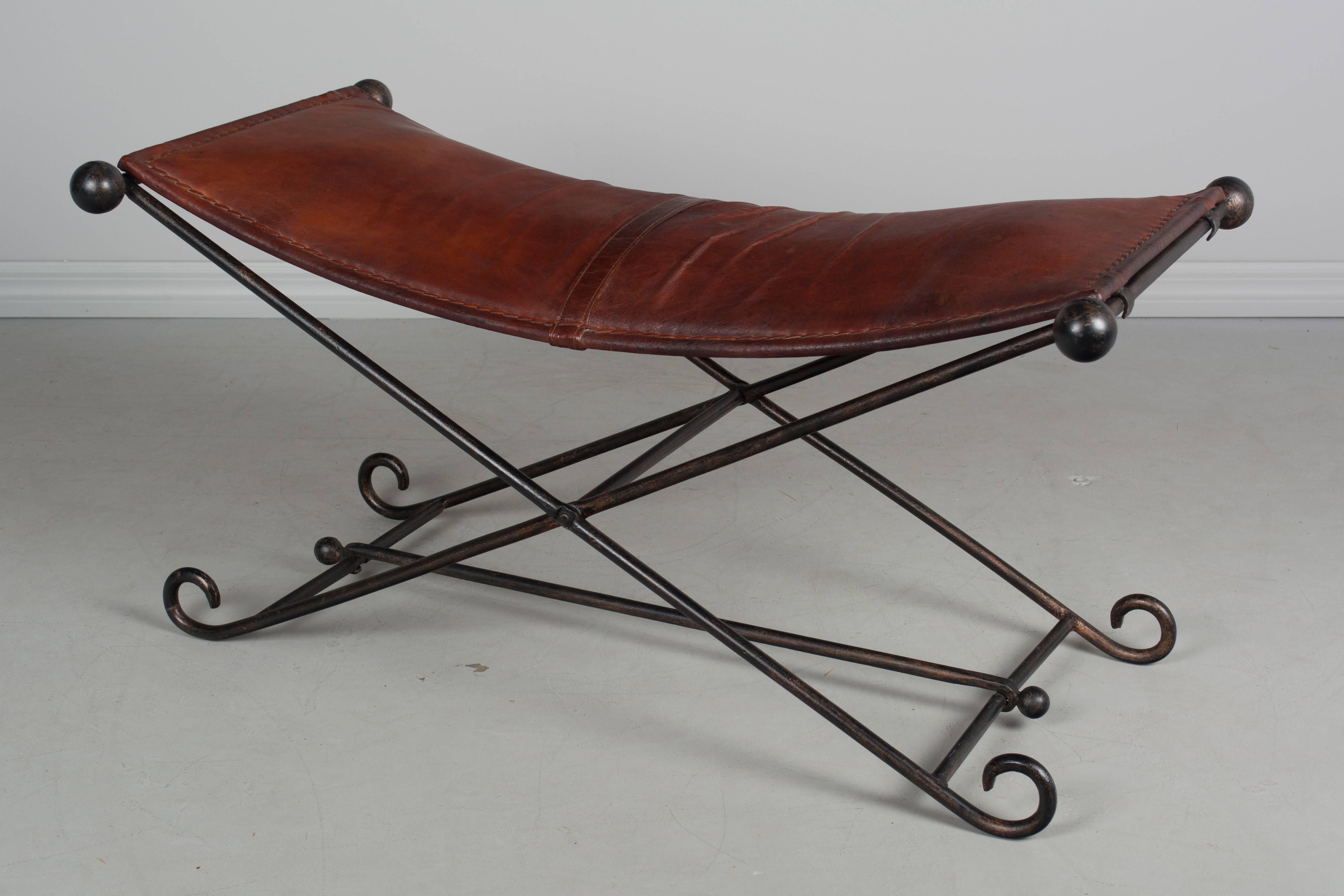 A Mid-Century Campaign style wrought iron X-form folding bench. Leather seat has a wonderful old patina with thick stitching. Iron has a dark bronze painted finish. Very sturdy and practical, this bench folds up for easy storage when not in use.