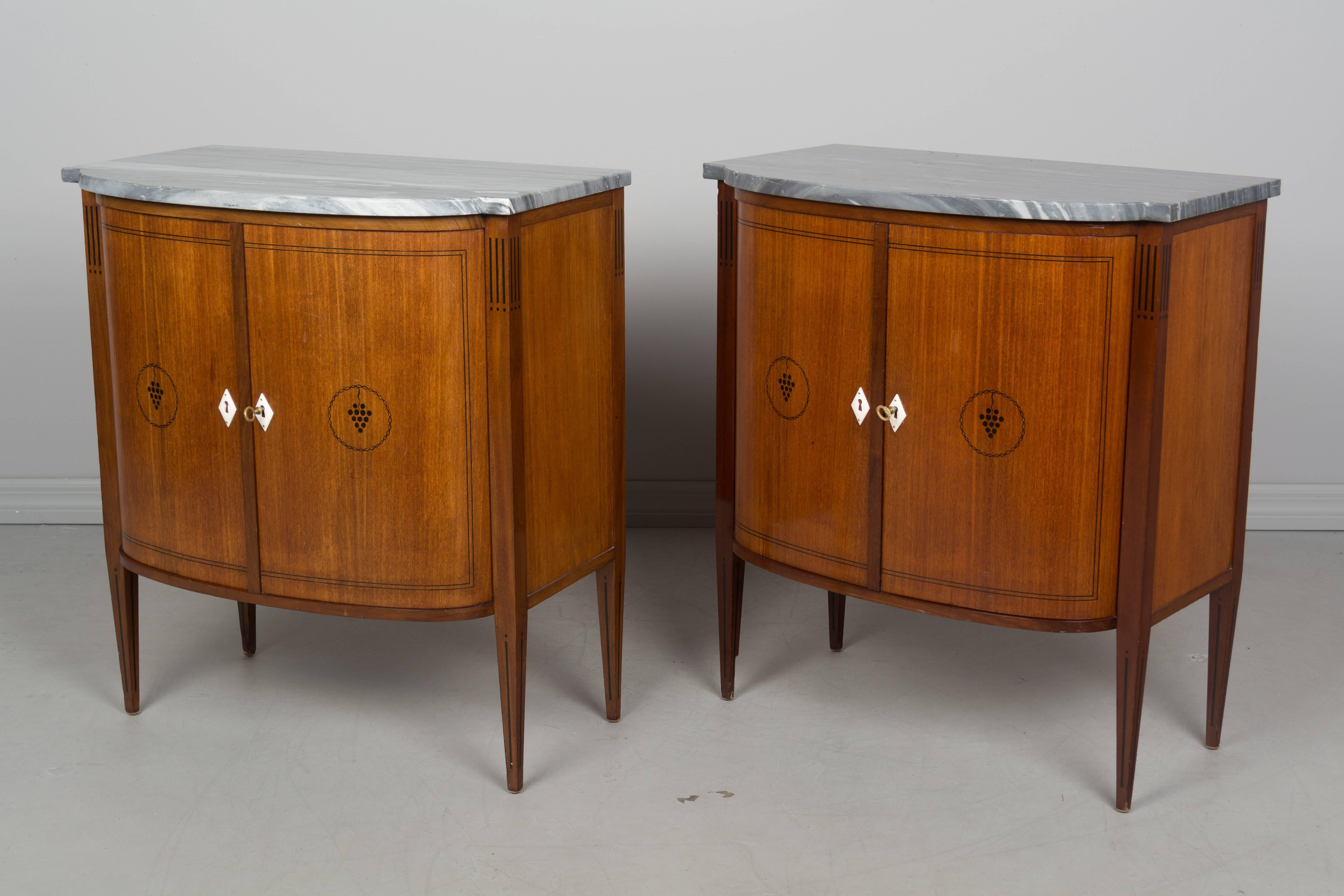 A pair of French Art Deco style cabinets, or side tables, made by Maison Krieger. Stamped below marble, circa 1940-1950s. Made of mahogany with curved front doors and original marble tops. Working locks and keys. Opening to one shelf. Very high