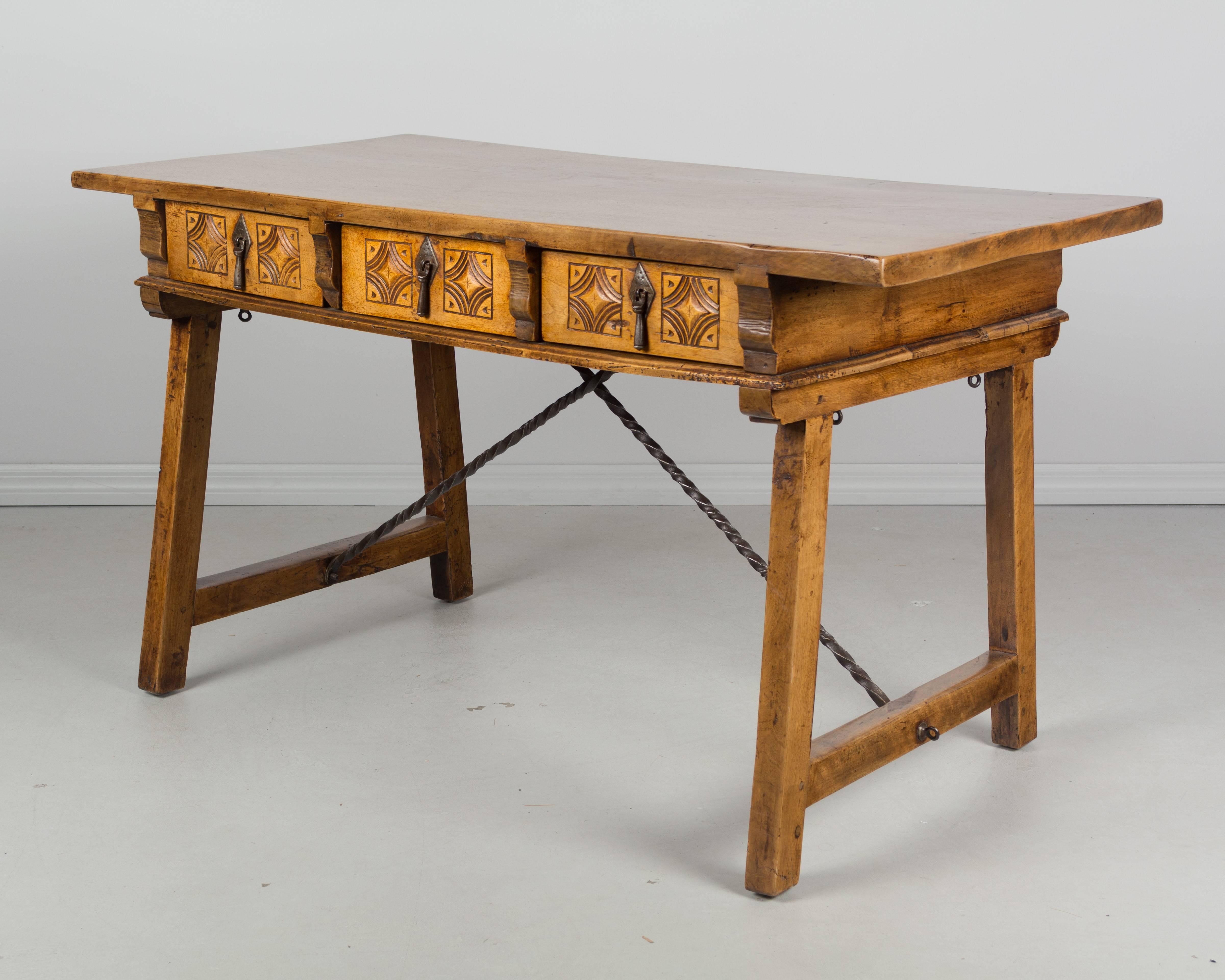 Spanish Baroque style table made of walnut with iron stretcher. Three dovetailed drawers with iron pulls. Top is constructed of one solid 1-1/2 inch thick plank of walnut. Note a patch on the back where there was a knot in the wood. Hand-carved