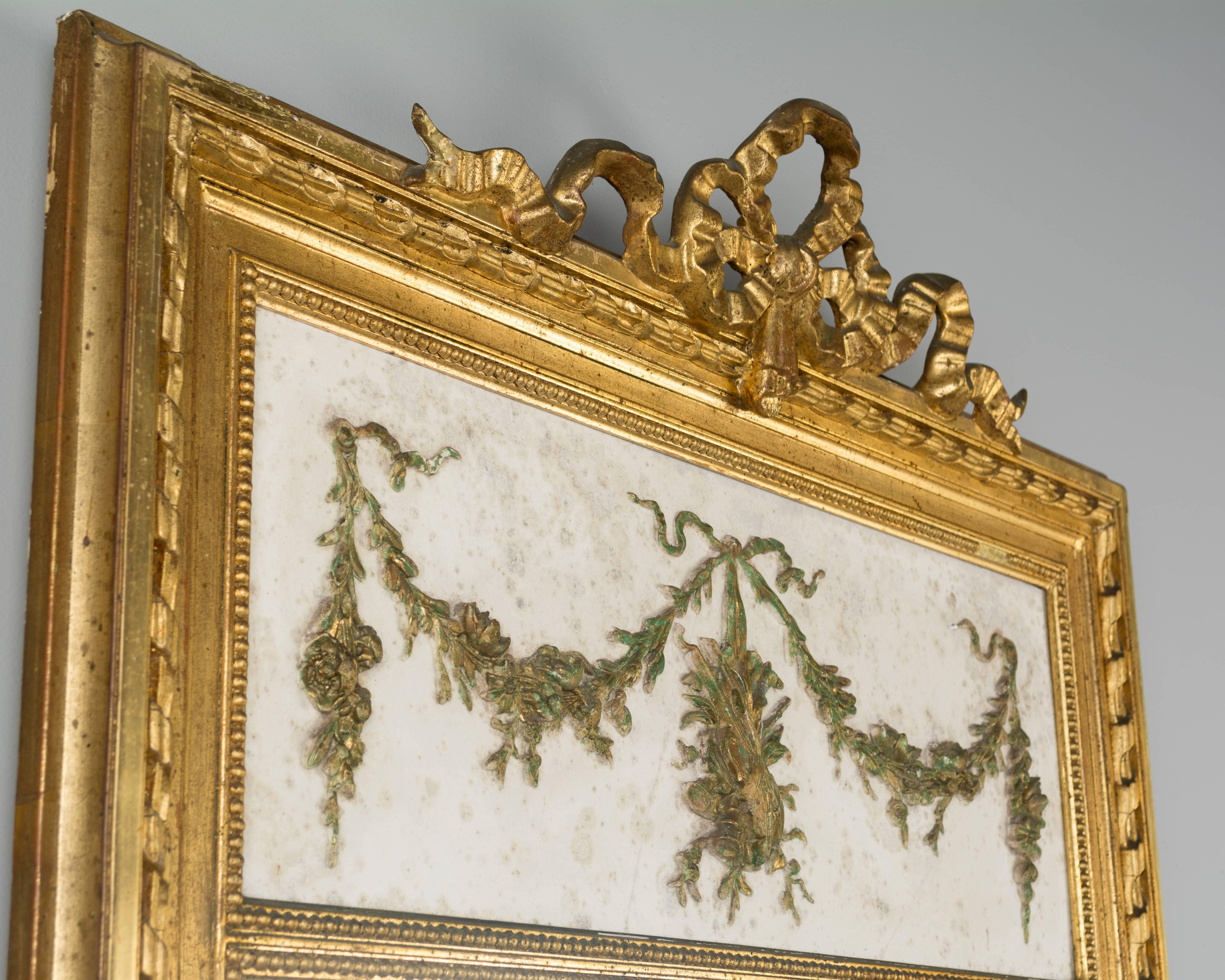 19th century Louis XVI style French gilded trumeau mirror. White marble with decorative bronze frieze in low relief depicting a floral garland with musical instruments. Gilt ribbon crown. Original beveled mirror. Nice verdigris patina to the bronze