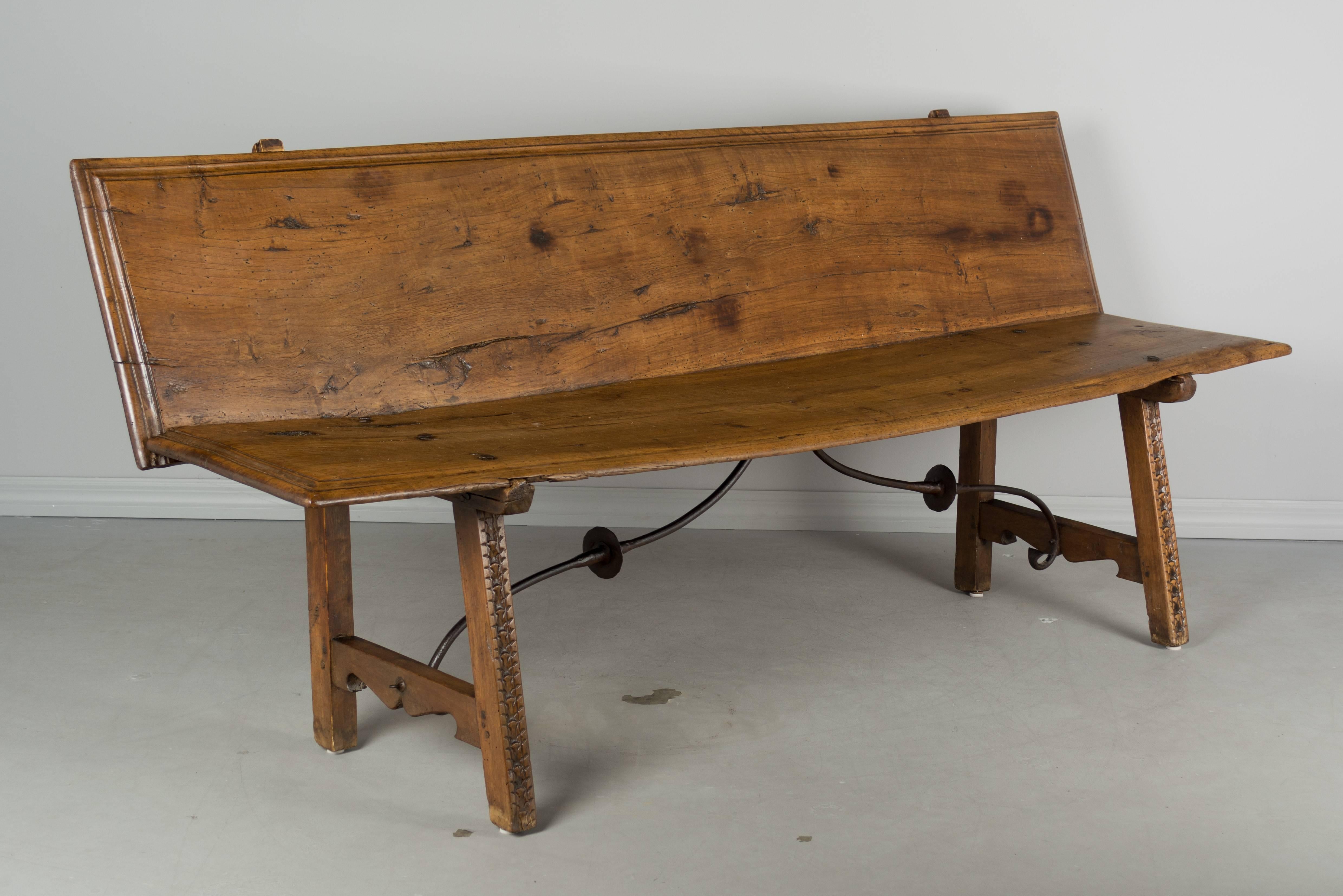 18th century Spanish Baroque style bench made from two solid walnut planks. Beautiful character to the wood with nice grain and natural knots. Waxed finish. Subtle hand-carved detail on the front of the legs. Wrought iron stretcher. Very sturdy with